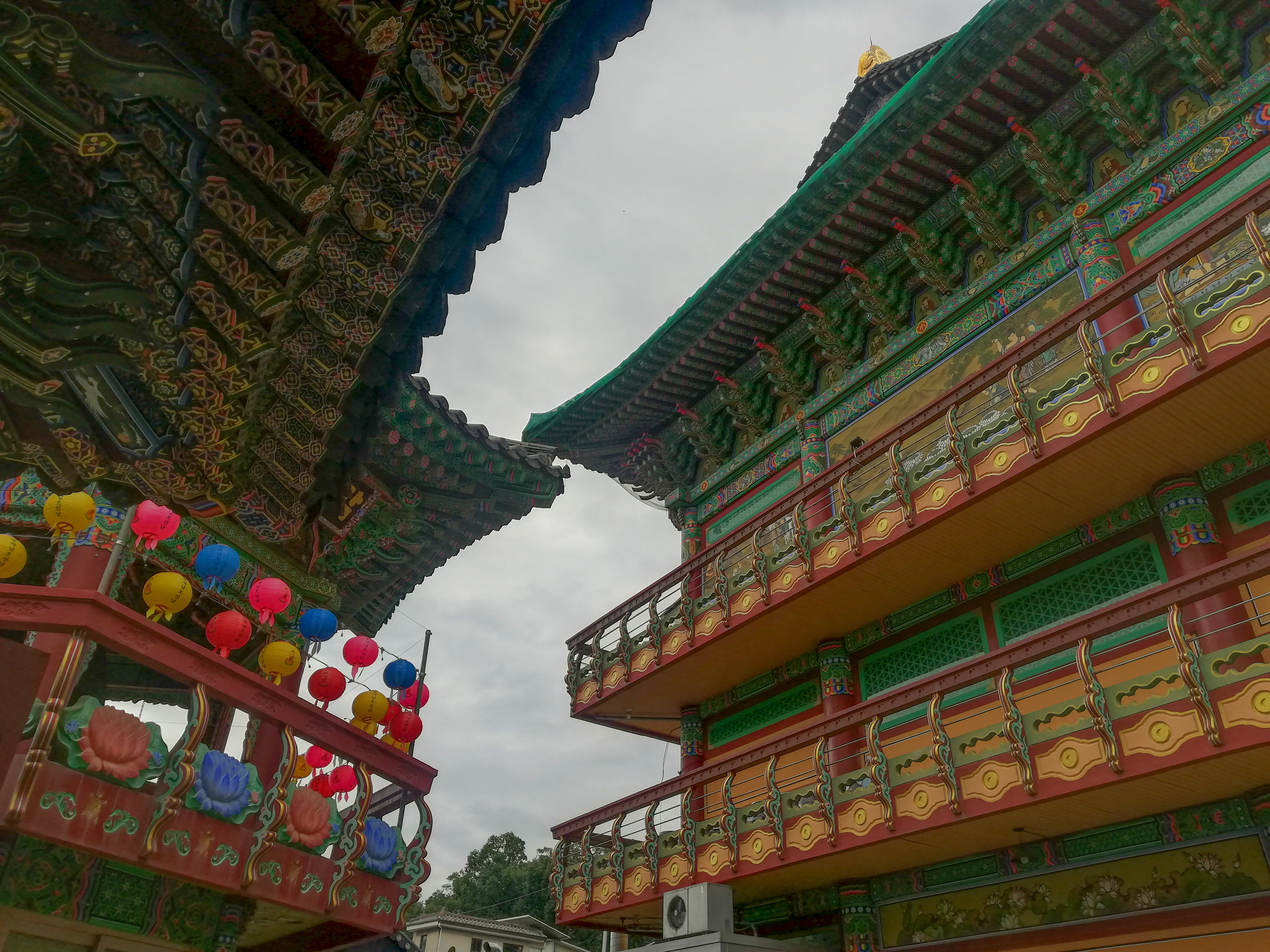 View of the exterior of a colorful temple with paper lanterns under cloudy skies