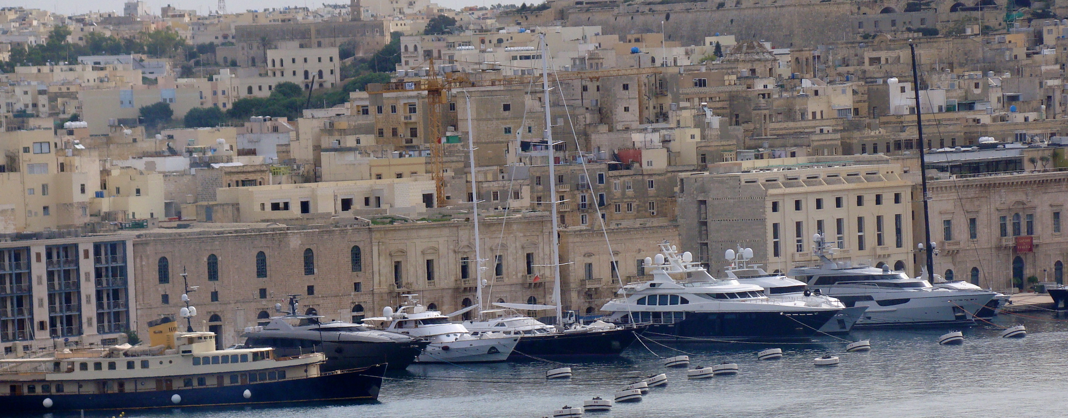 View from the water of several large yachts docked in a port city full of old buildings