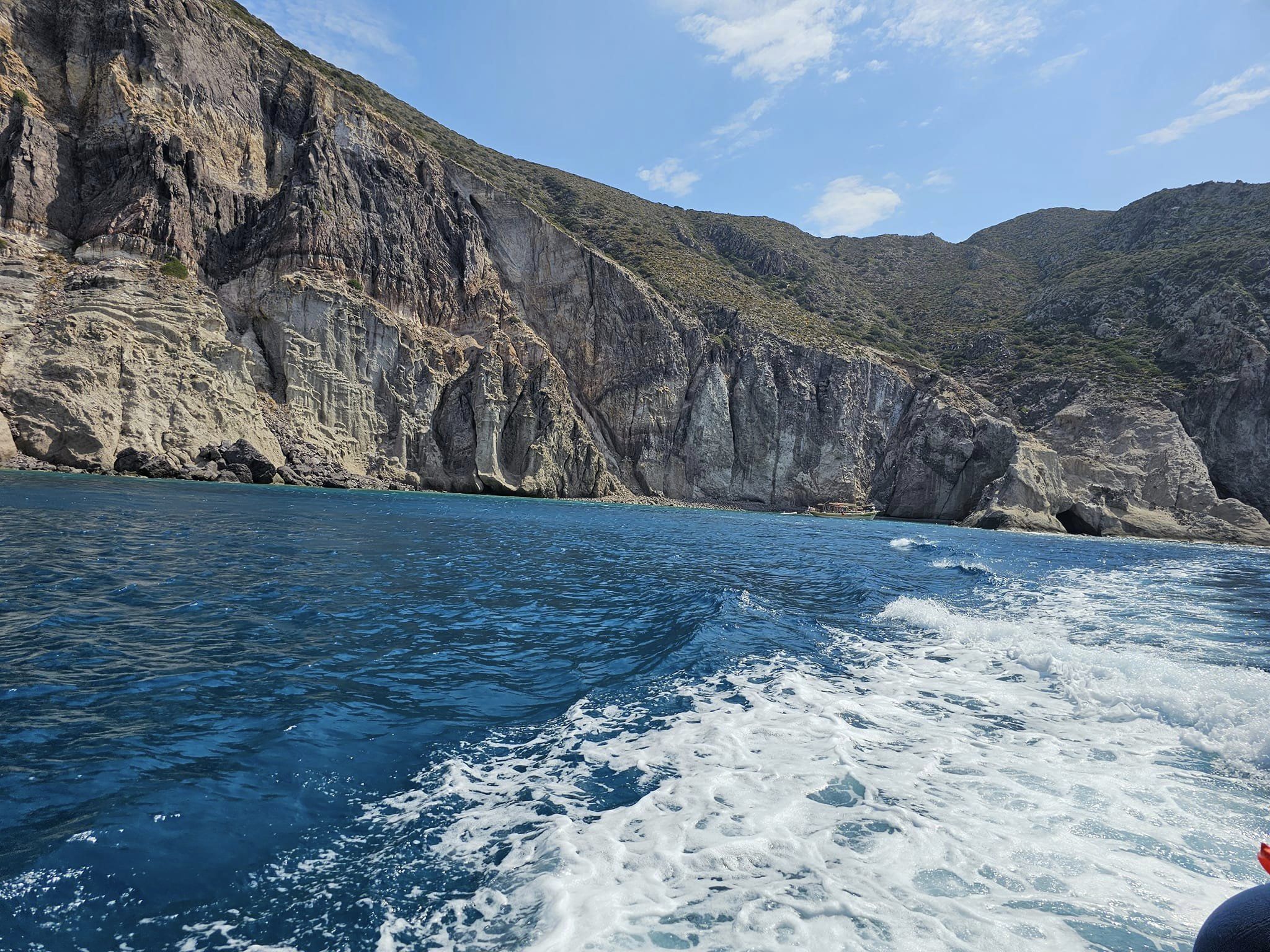 Waves lap a rocky shore on a bright day dotted with clouds.