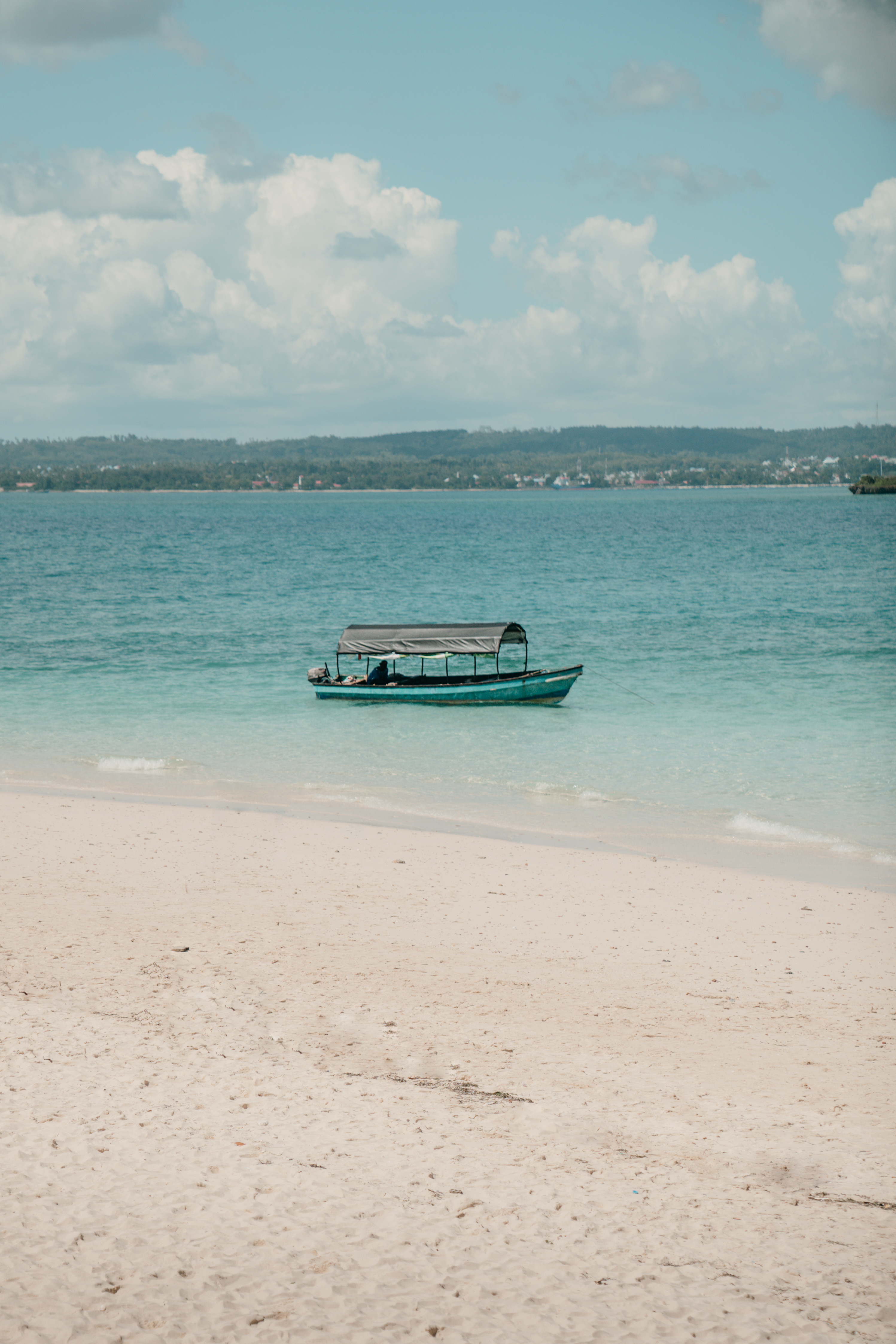 A boat floats on crystal clear waters as gentle waves lap the shore on a sunny day.