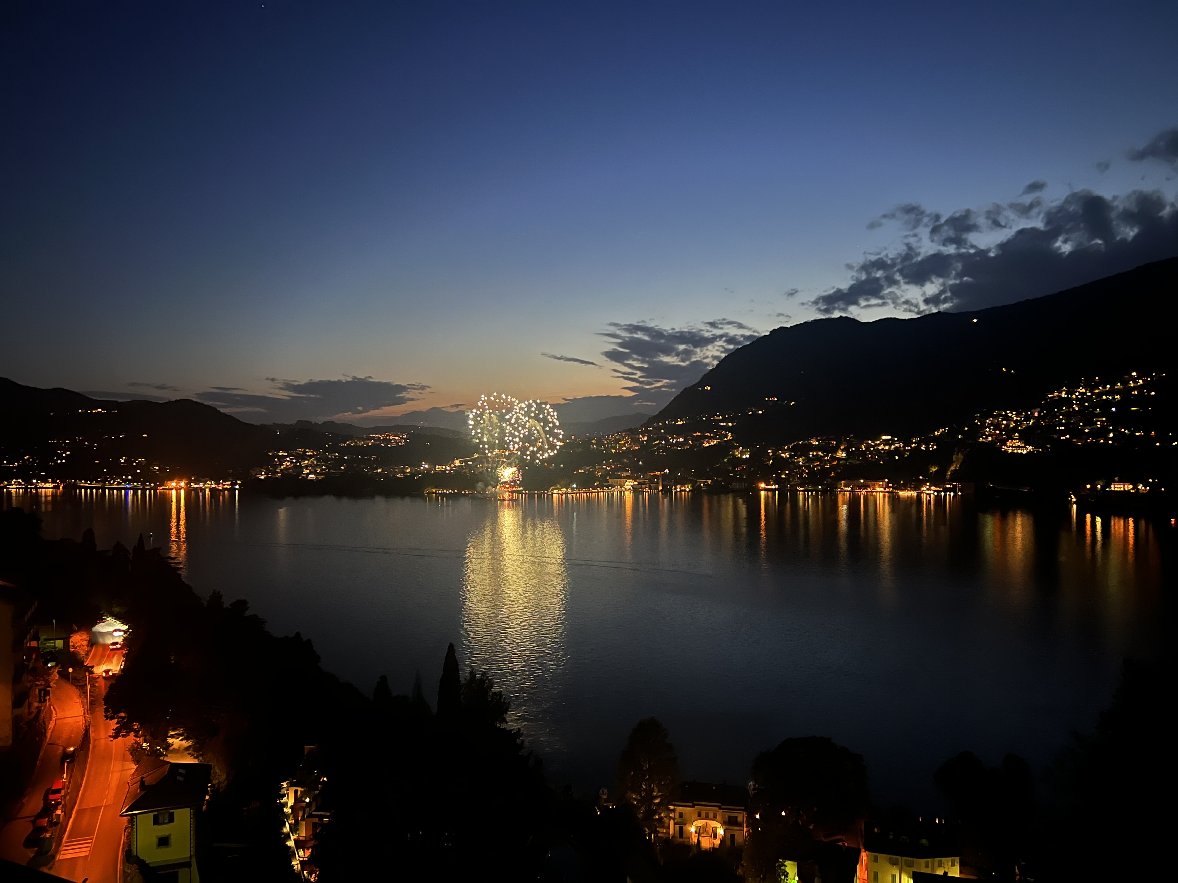 Colorful fireworks lighting up the night sky over Lake Como, creating a stunning reflection on the water below.
