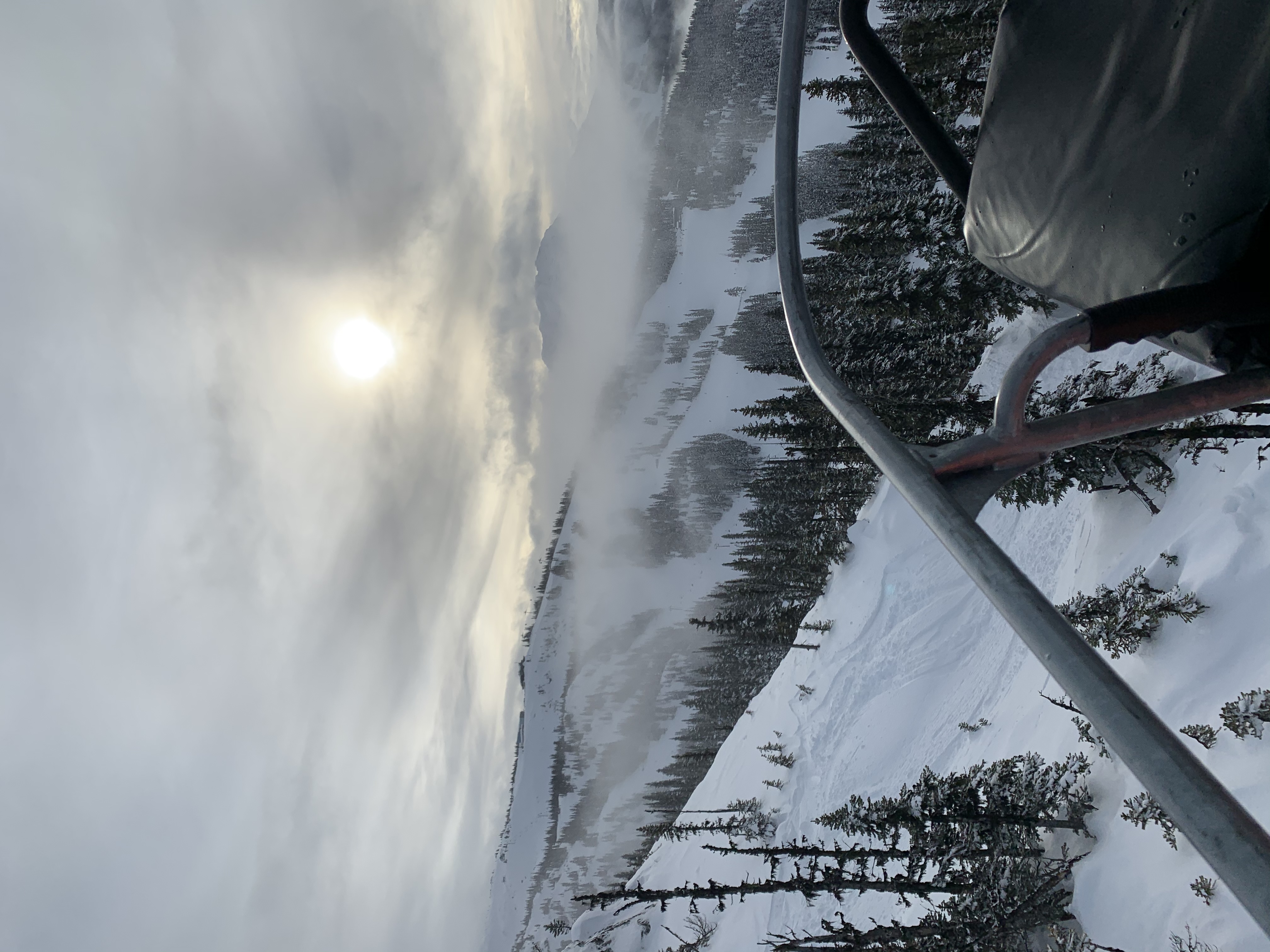 Snowy mountain landscape with a ski lift, trees and distant mountains.