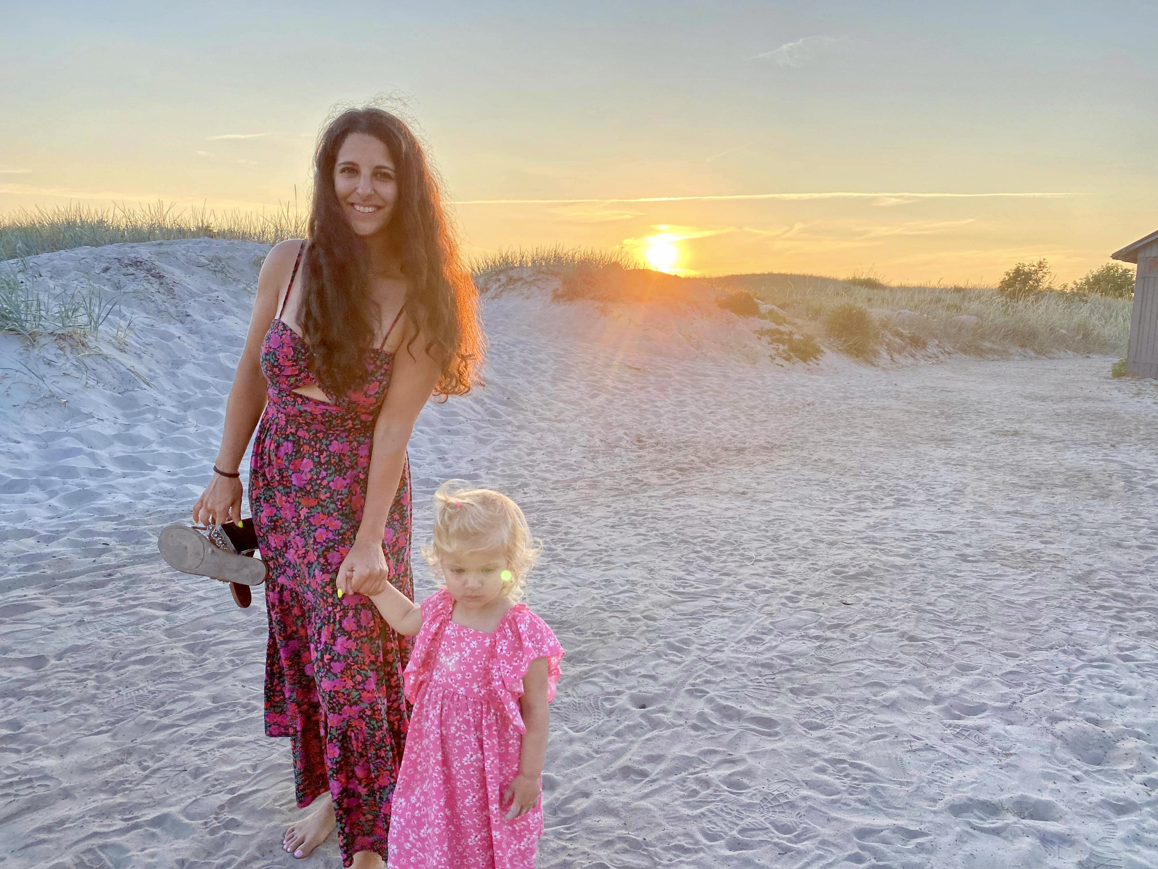 Advisor posing on the beach in a dress holding a little girl's hand.