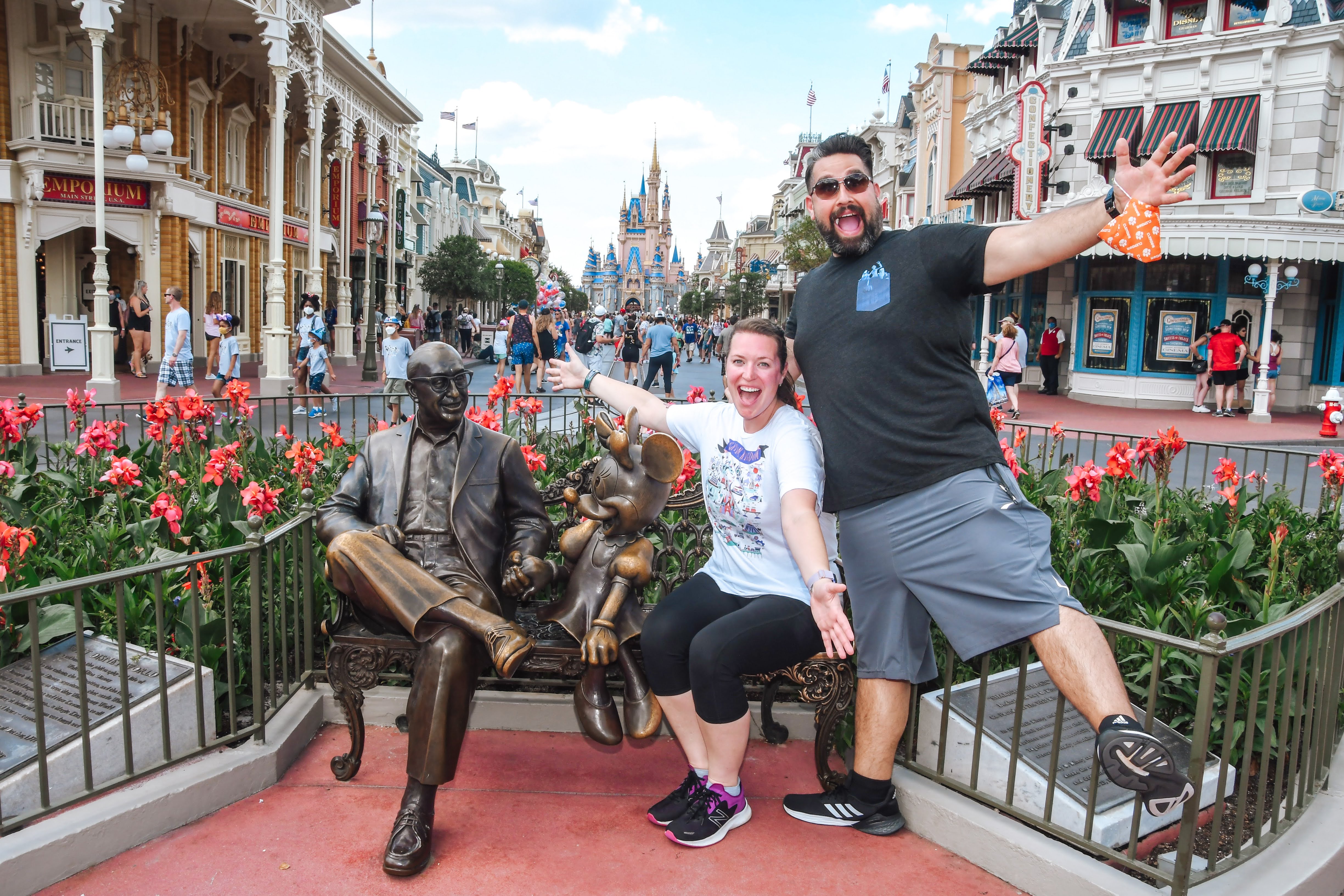 Beth and her partner posing by a bronze statue of Walt Disney outdoors on a sunny day