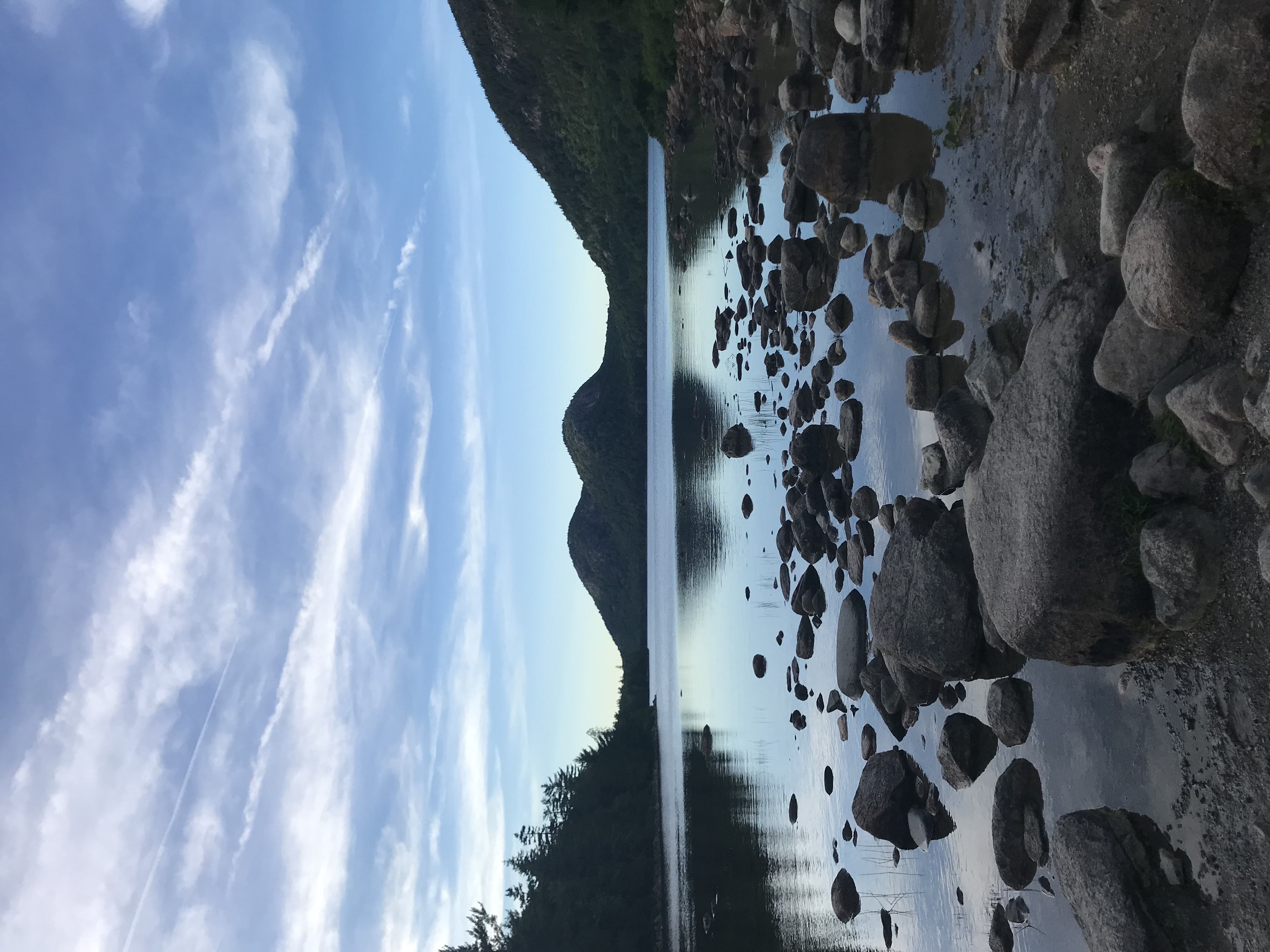 Beautiful view of rocks leading into a glassy lake surrounded by mountains under clear skies