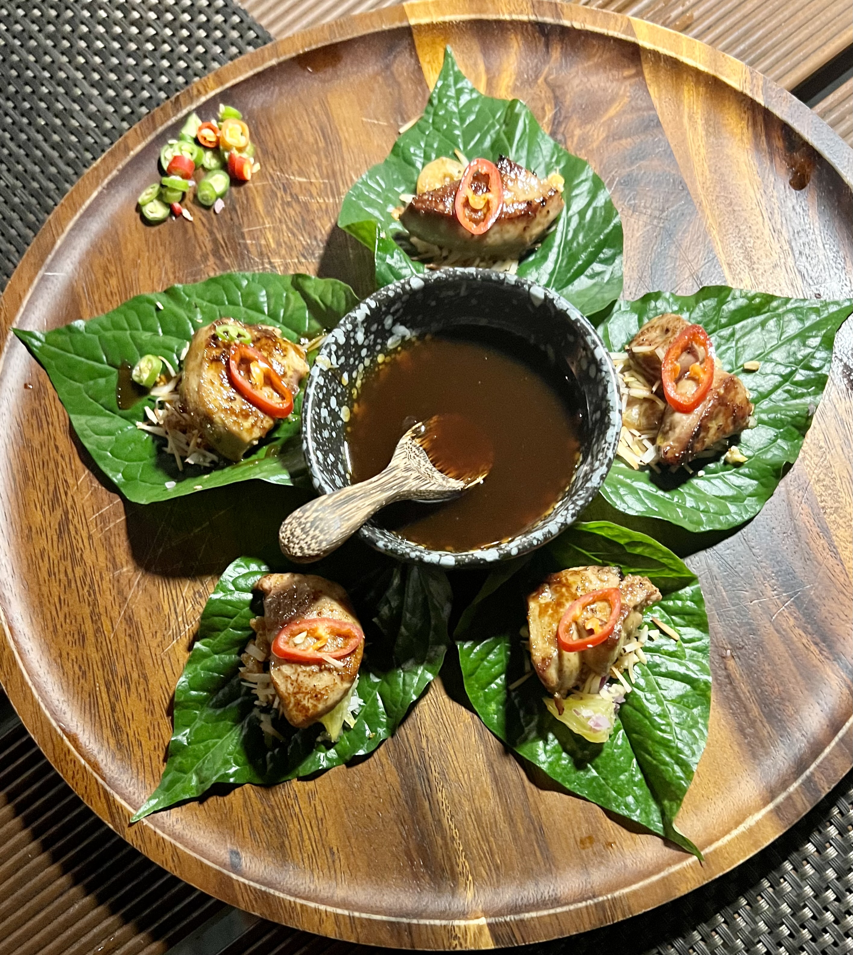 View of a wooden plate of food with a dish of sauce in the center