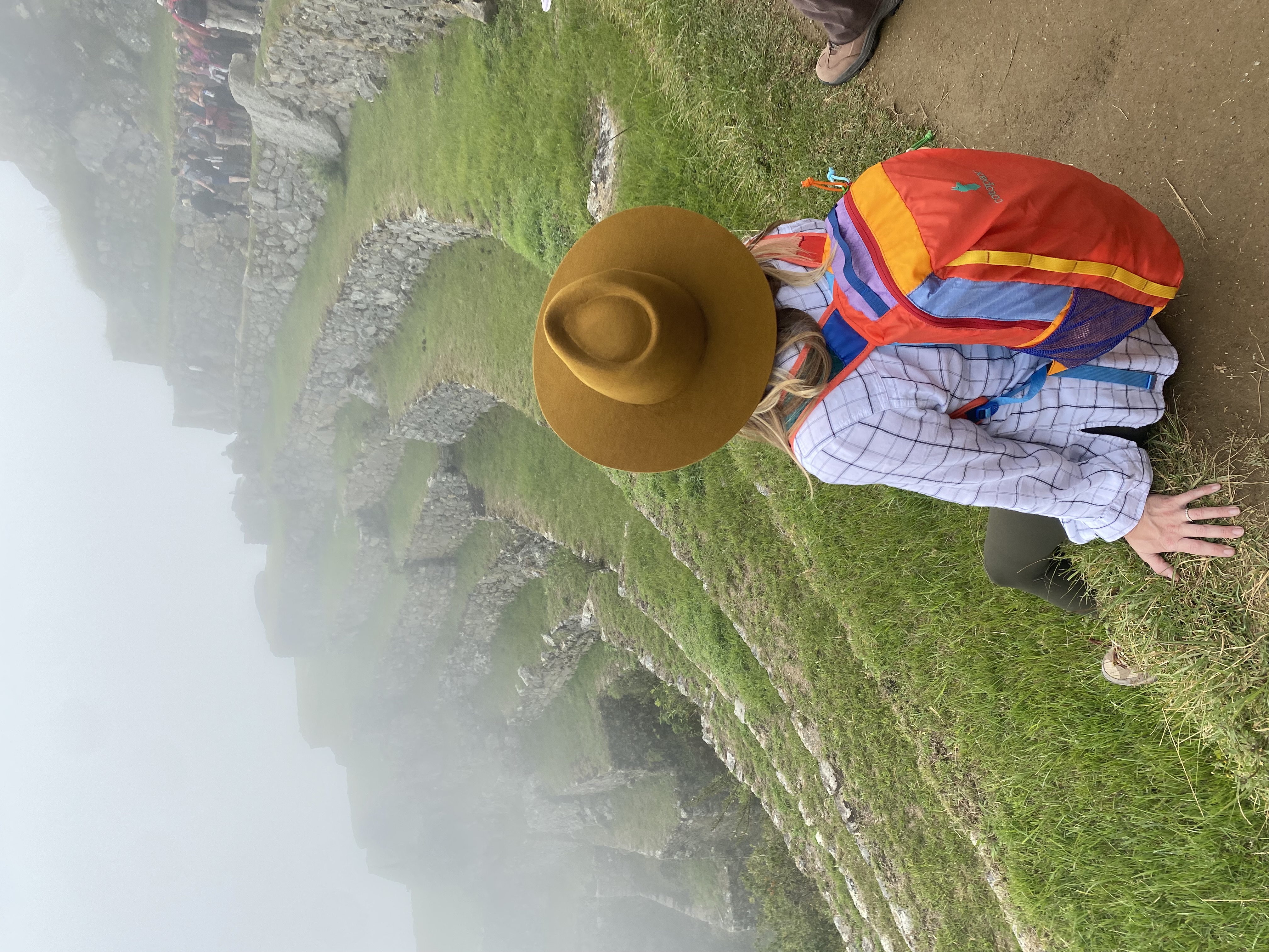 View of Angie wearing a colorful backpack on a tiered cliffside in foggy weather