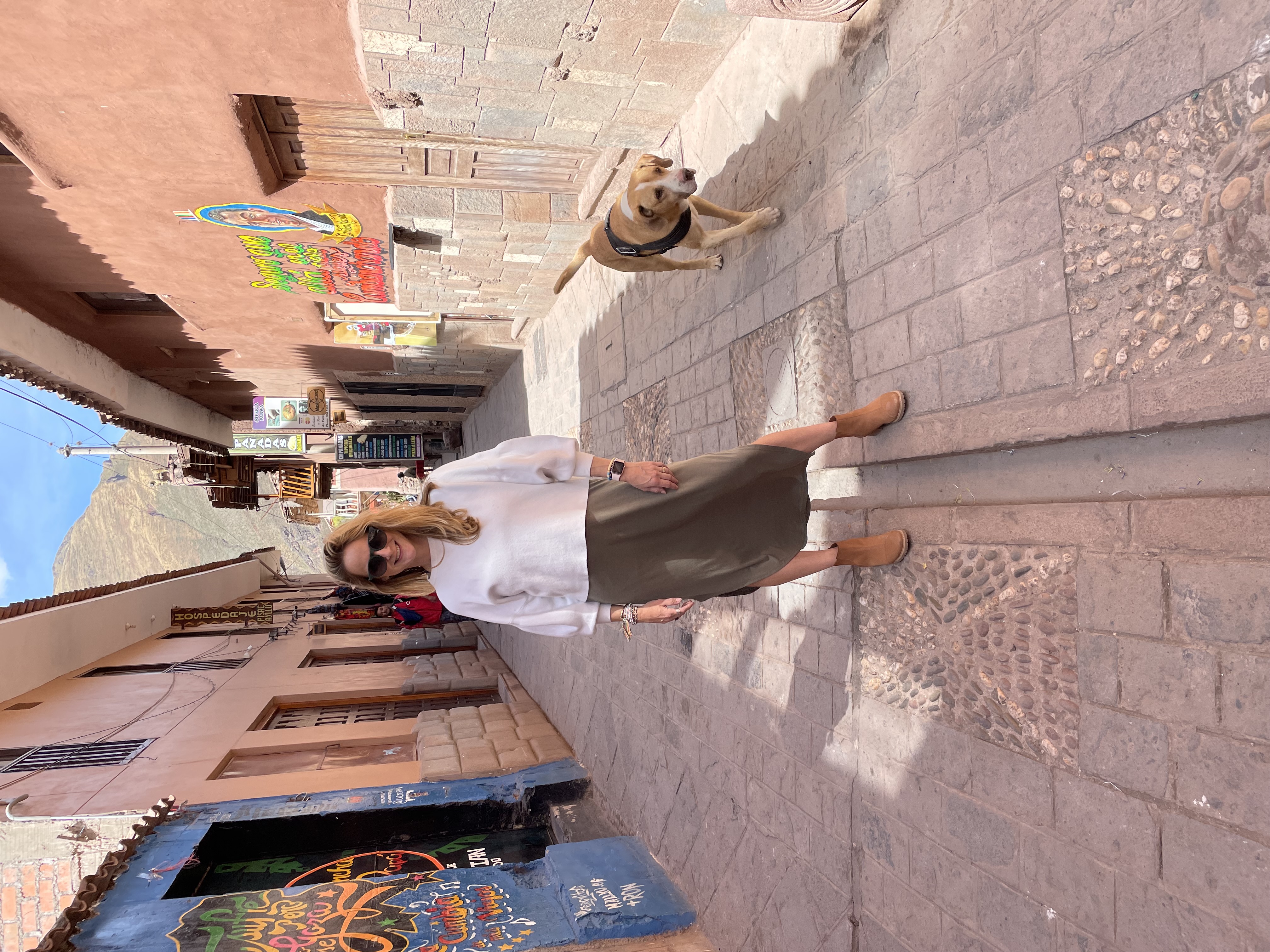 Angie posing in the middle of a narrow street with a dog next to her on a sunny day