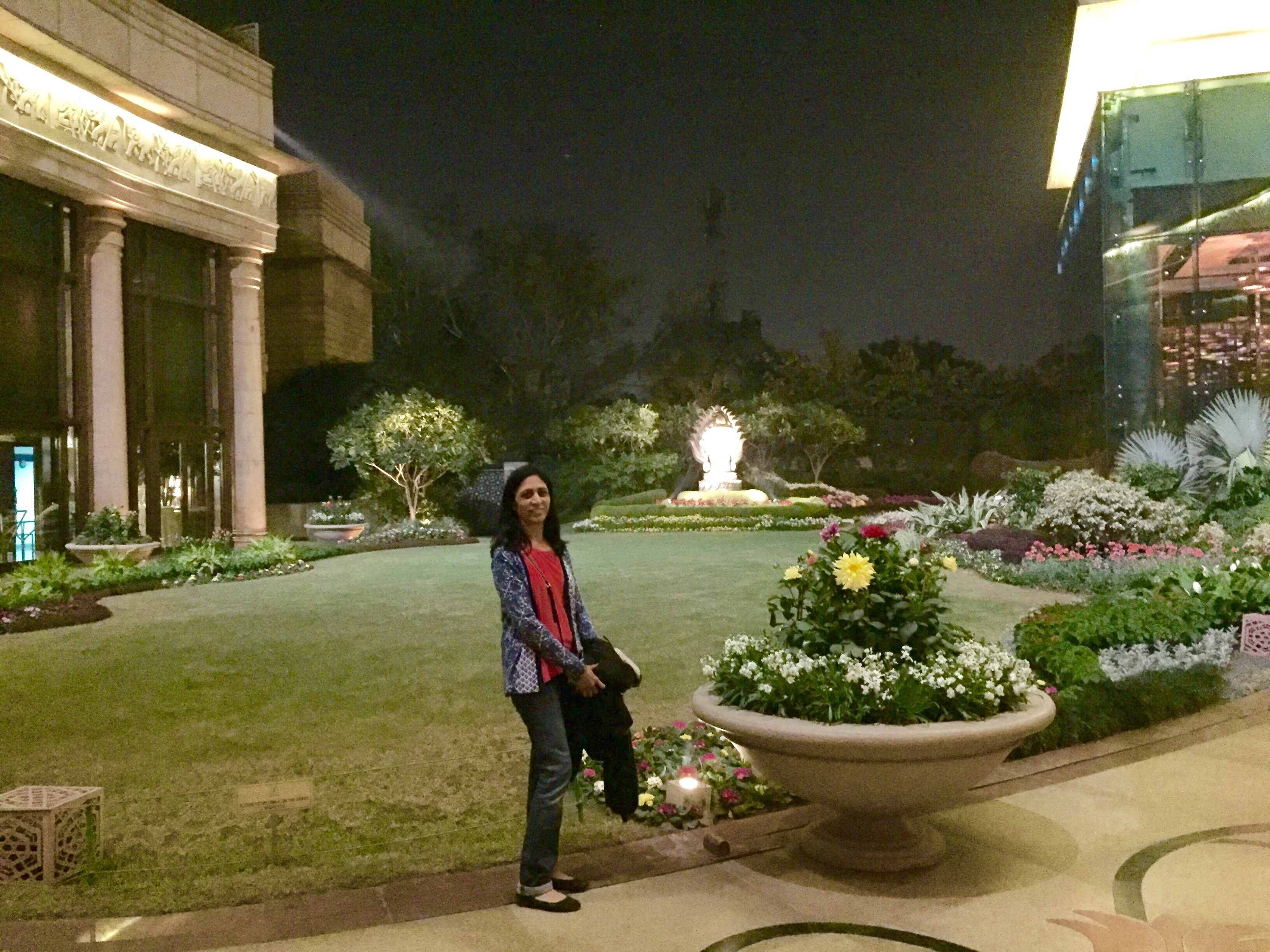 Della standing alone in a manicured garden at night