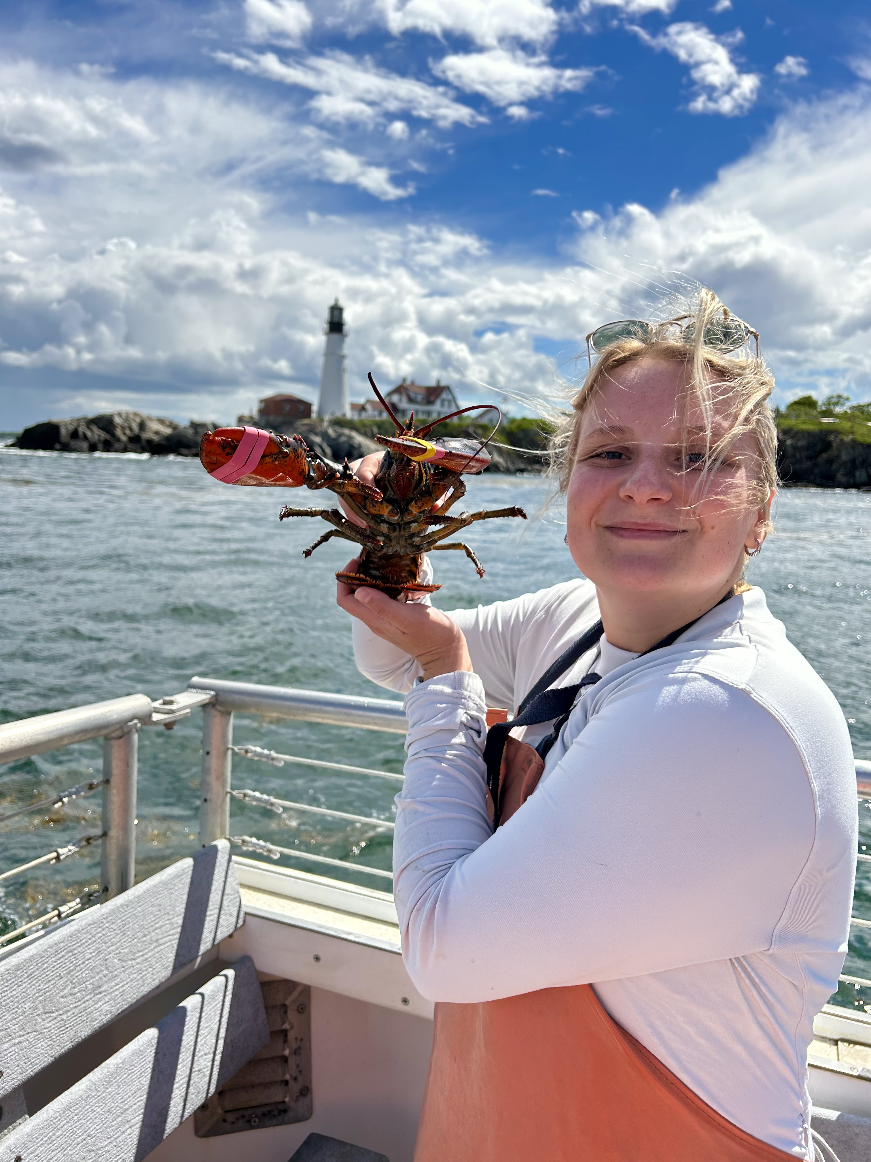 Advisor posing hold a lobster in her hand with the ocean in the background.