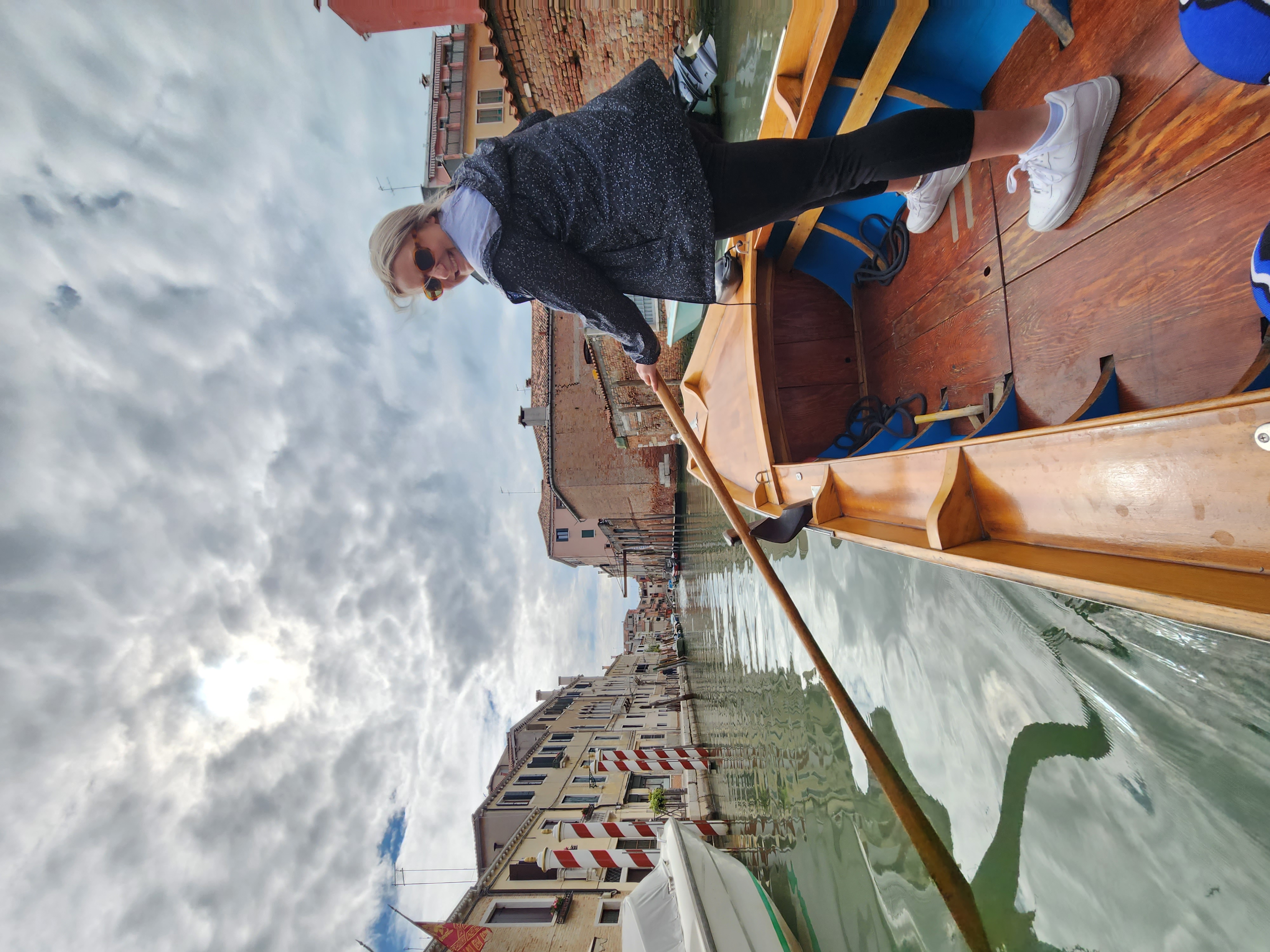 A woman rows a boat down a serene canal surrounded by lush greenery.