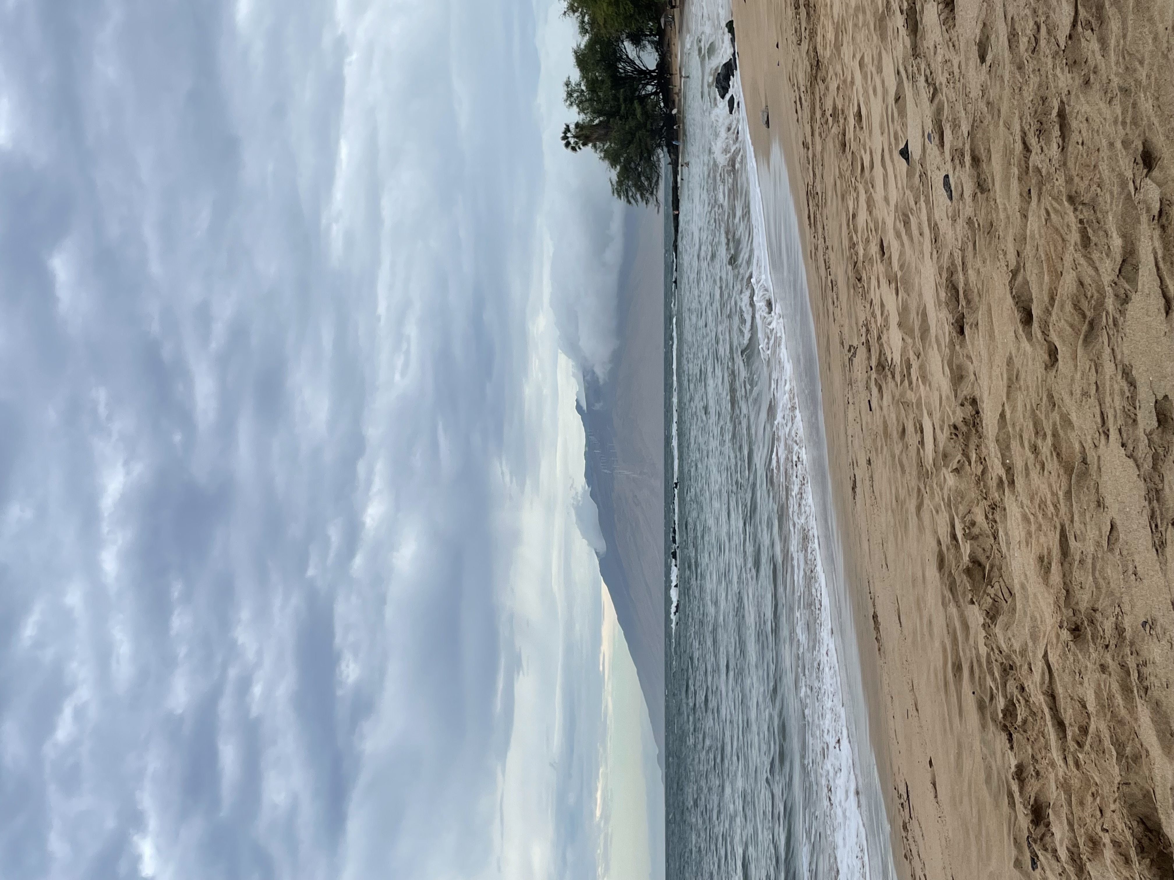 A view of the shoreline with a mountain range in the distance on a sunny day.