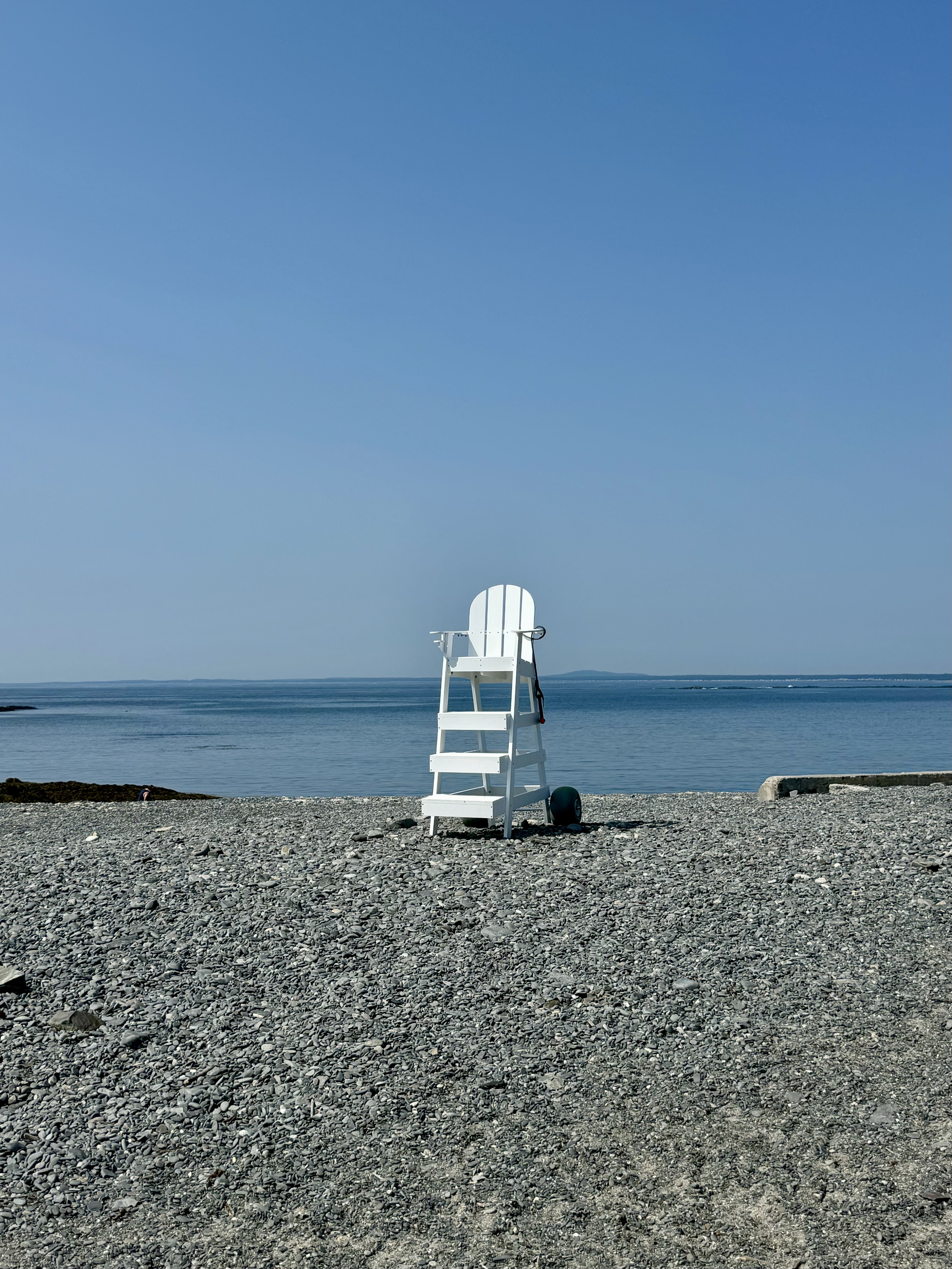 A lifeguard chair on a beach with the ocean in the distance on a sunny day.