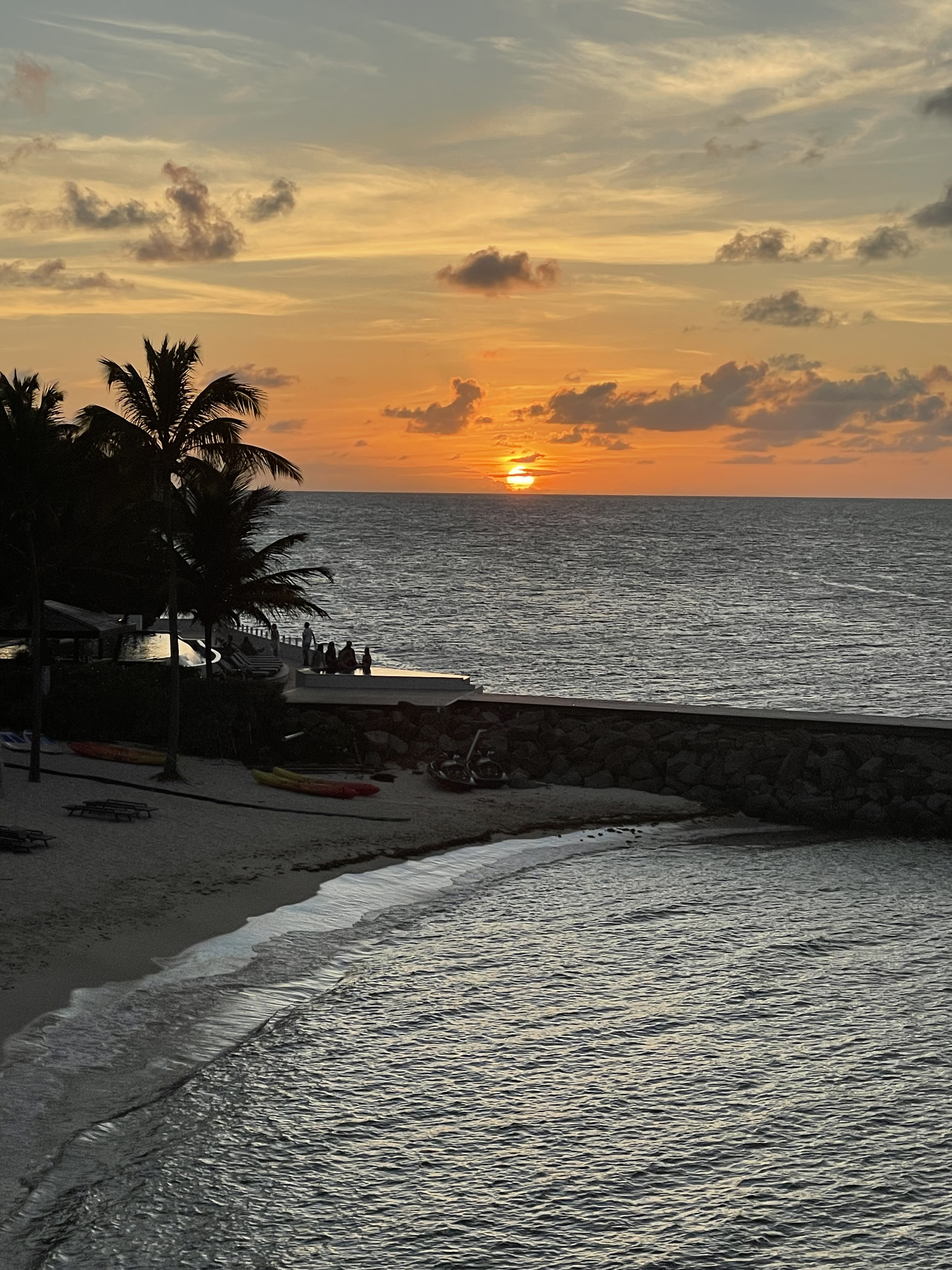 An orange sky frames the sun as it dips below rolling ocean waves on a clear day.