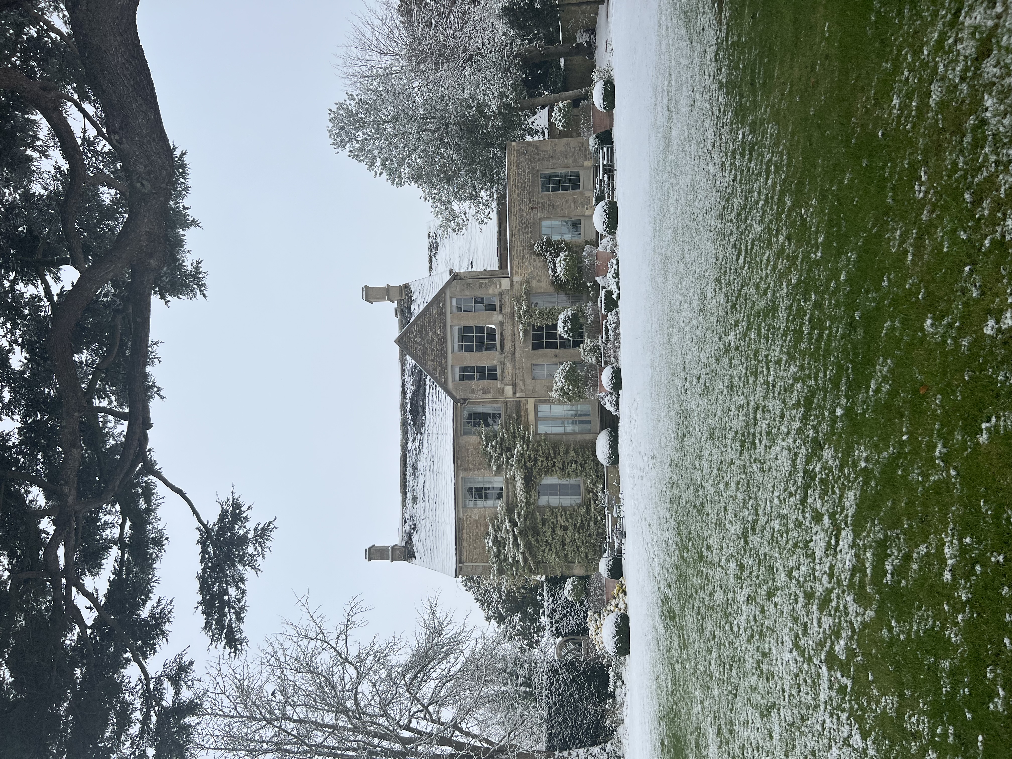 View of a pretty stone house and large yard dusted in snow