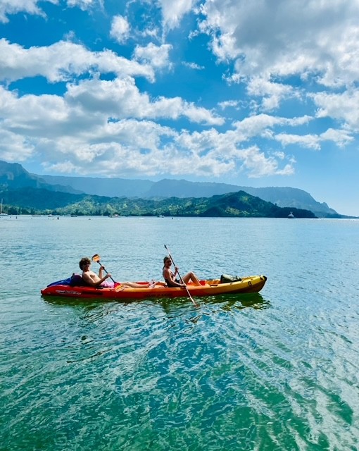 View of two people kayaking through clear water and beautiful mountains in the distance