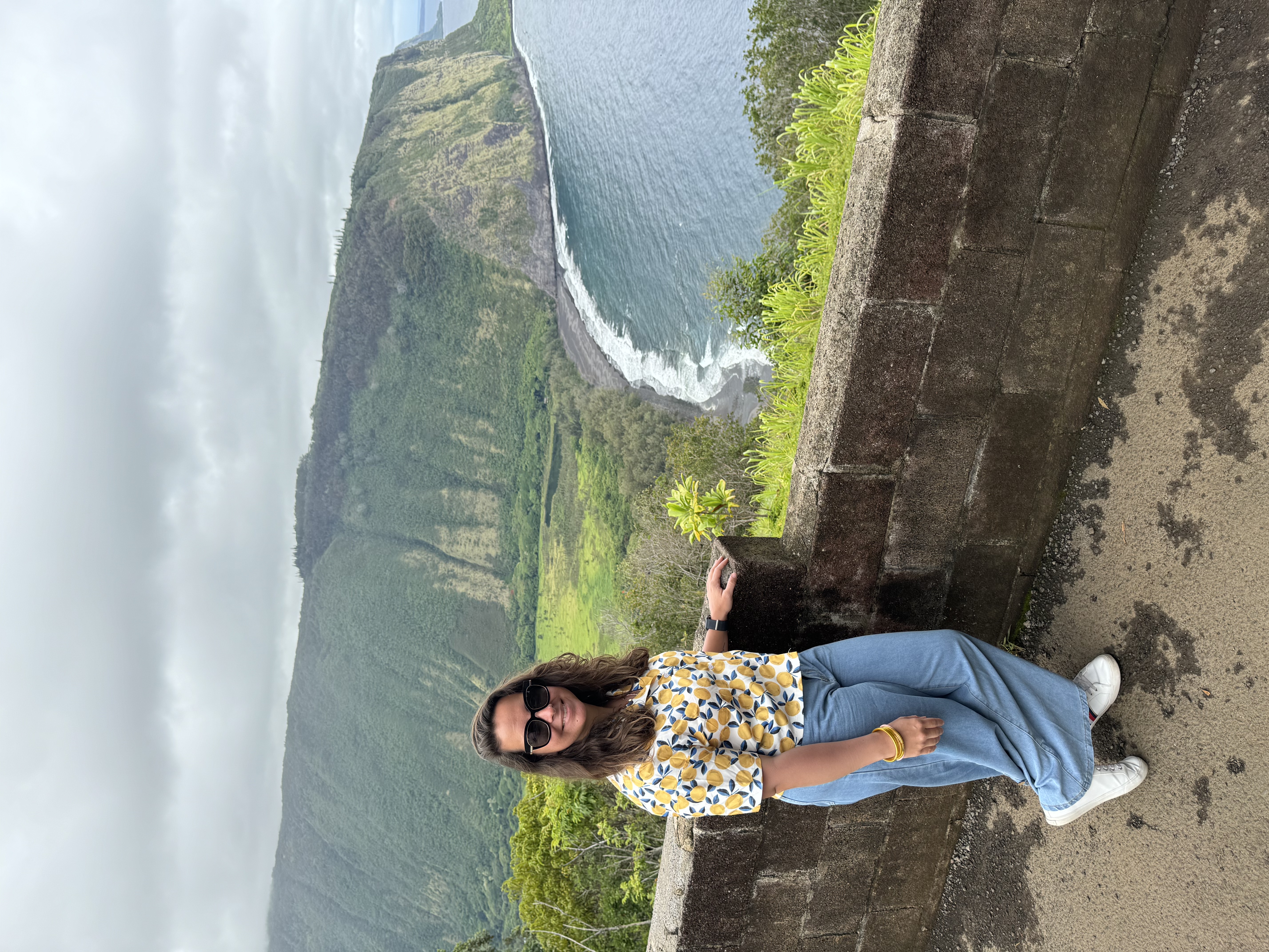 Sharon posing at a lookout point overlooking a beautiful coastal area with steep cliffs on a cloudy day
