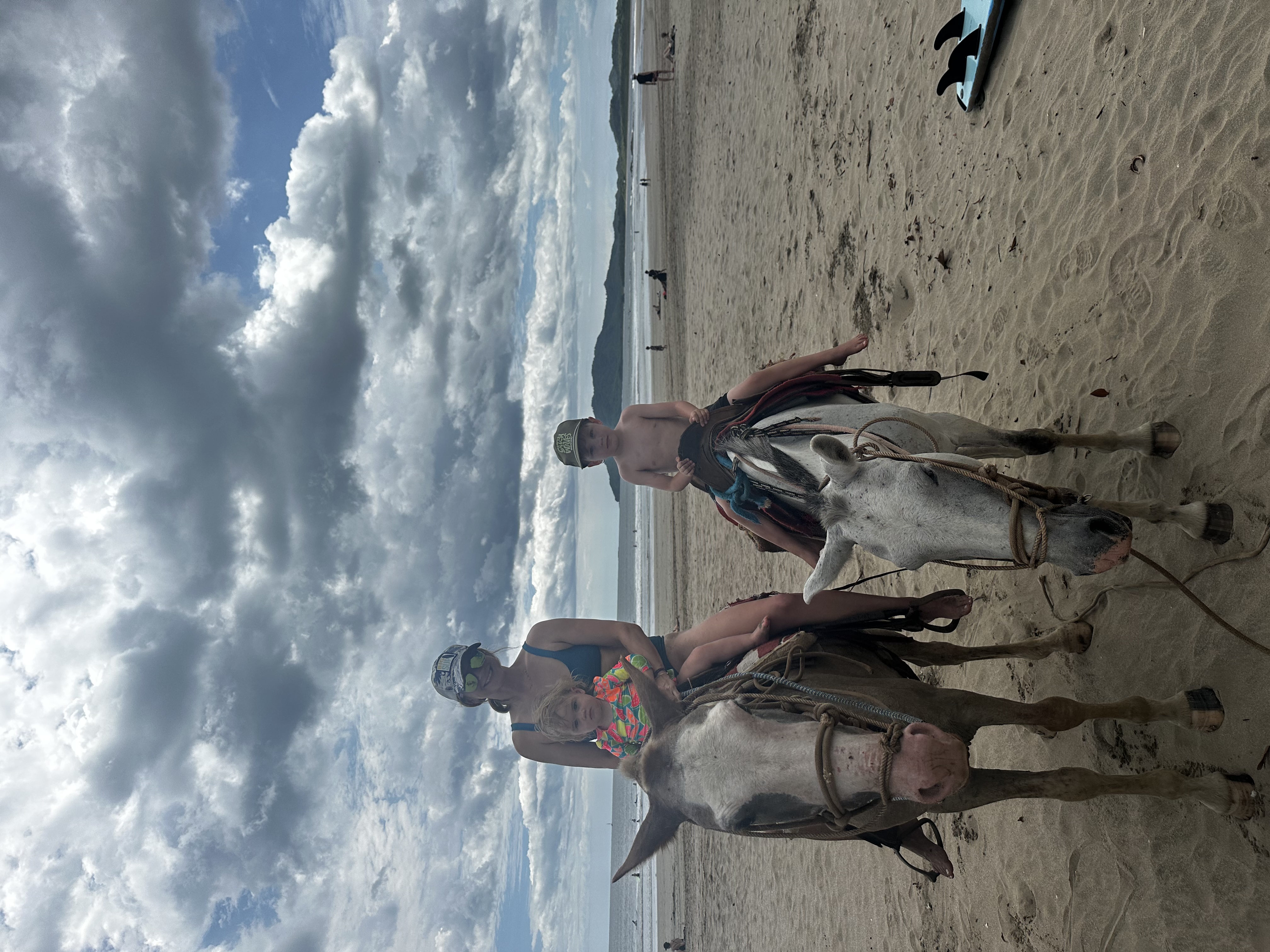Advisor and a young child on horseback on the beach on a cloudy day
