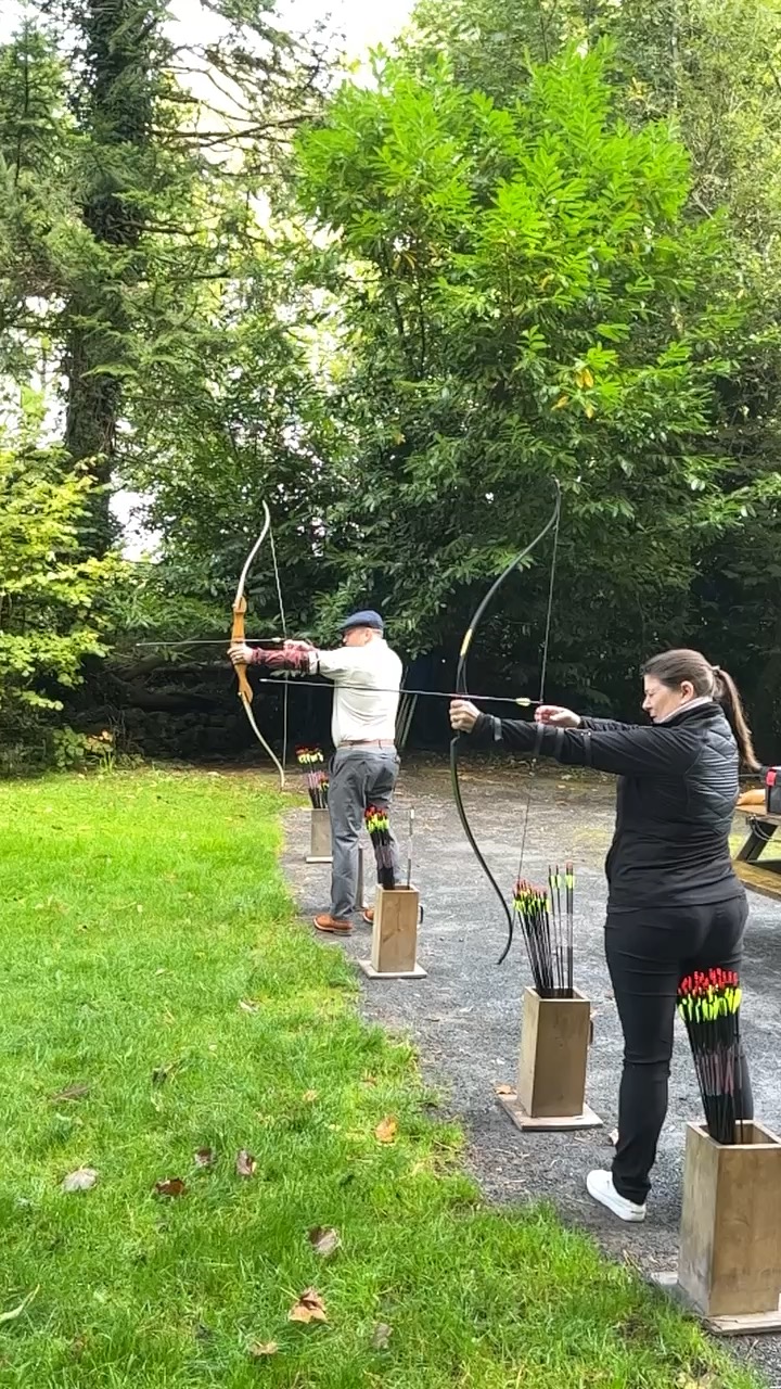 Leslie and a man shooting a bow and arrow outdoors