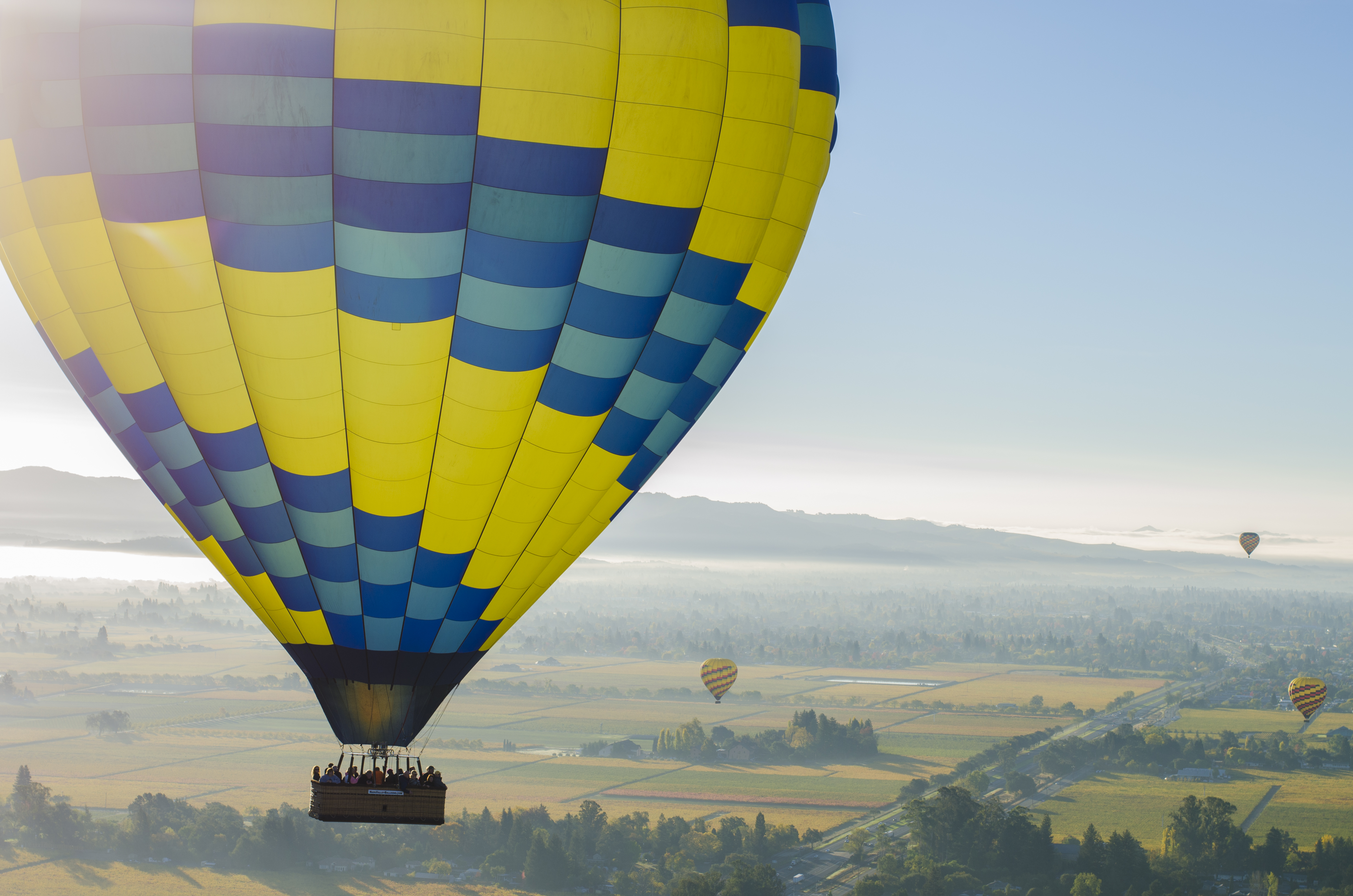 View of a yellow and blue hot air Mallon in the sky overlooking a beautiful green landscape
