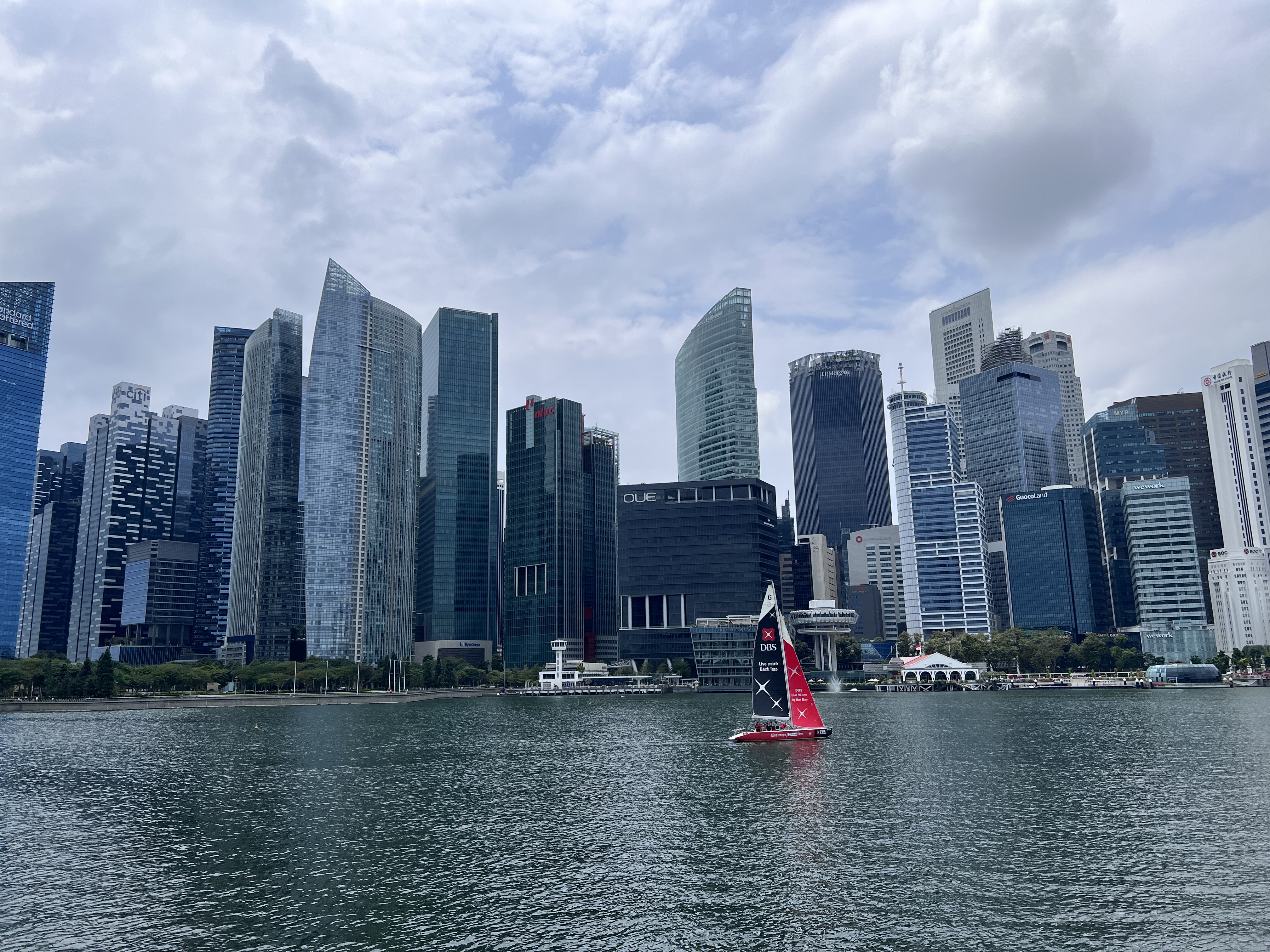 Skyscrapers reach toward the sky as water laps the shore on a cloudy day.