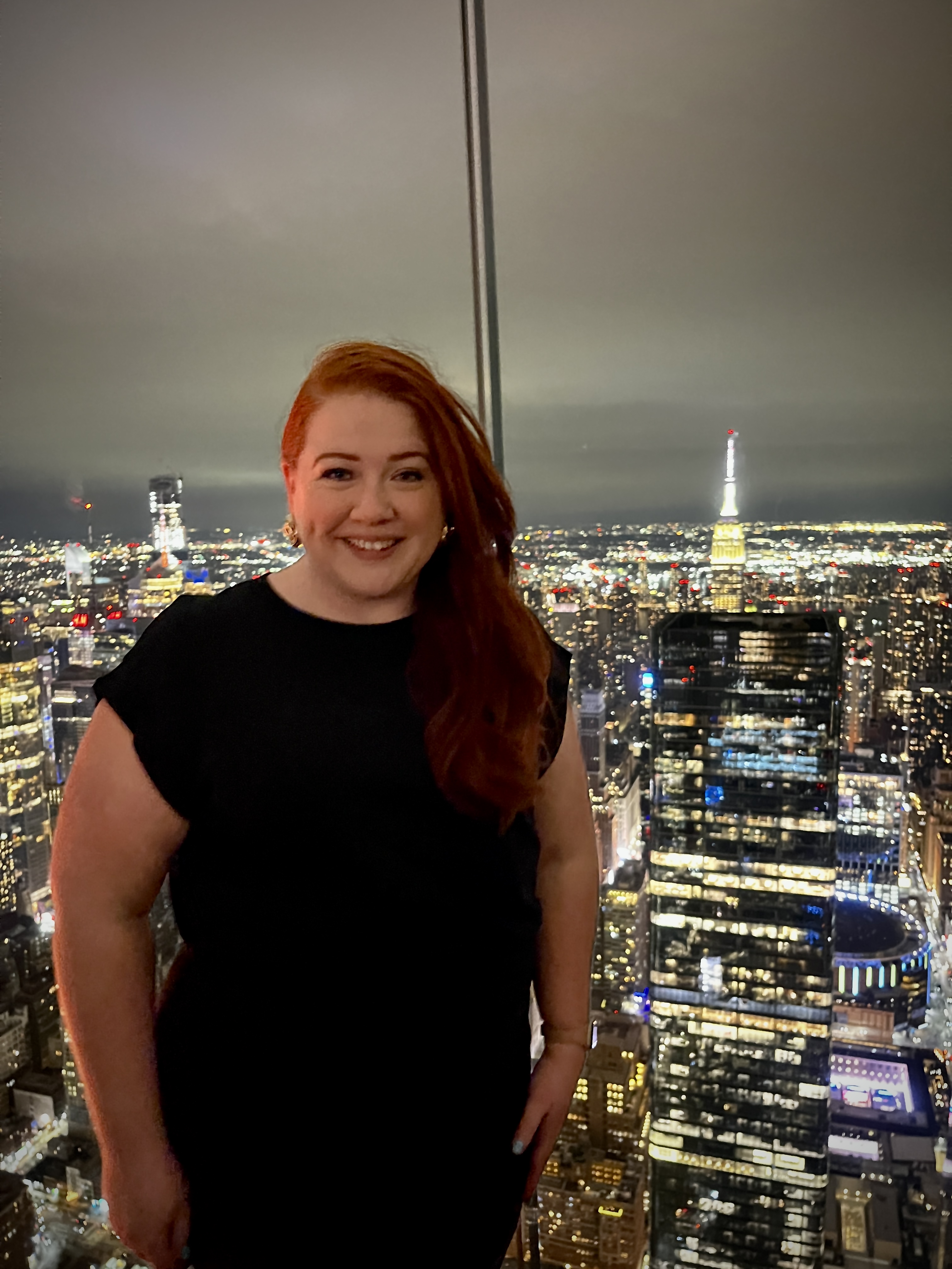 Advisor smiling in a black dress with a nighttime cityscape lit up behind her