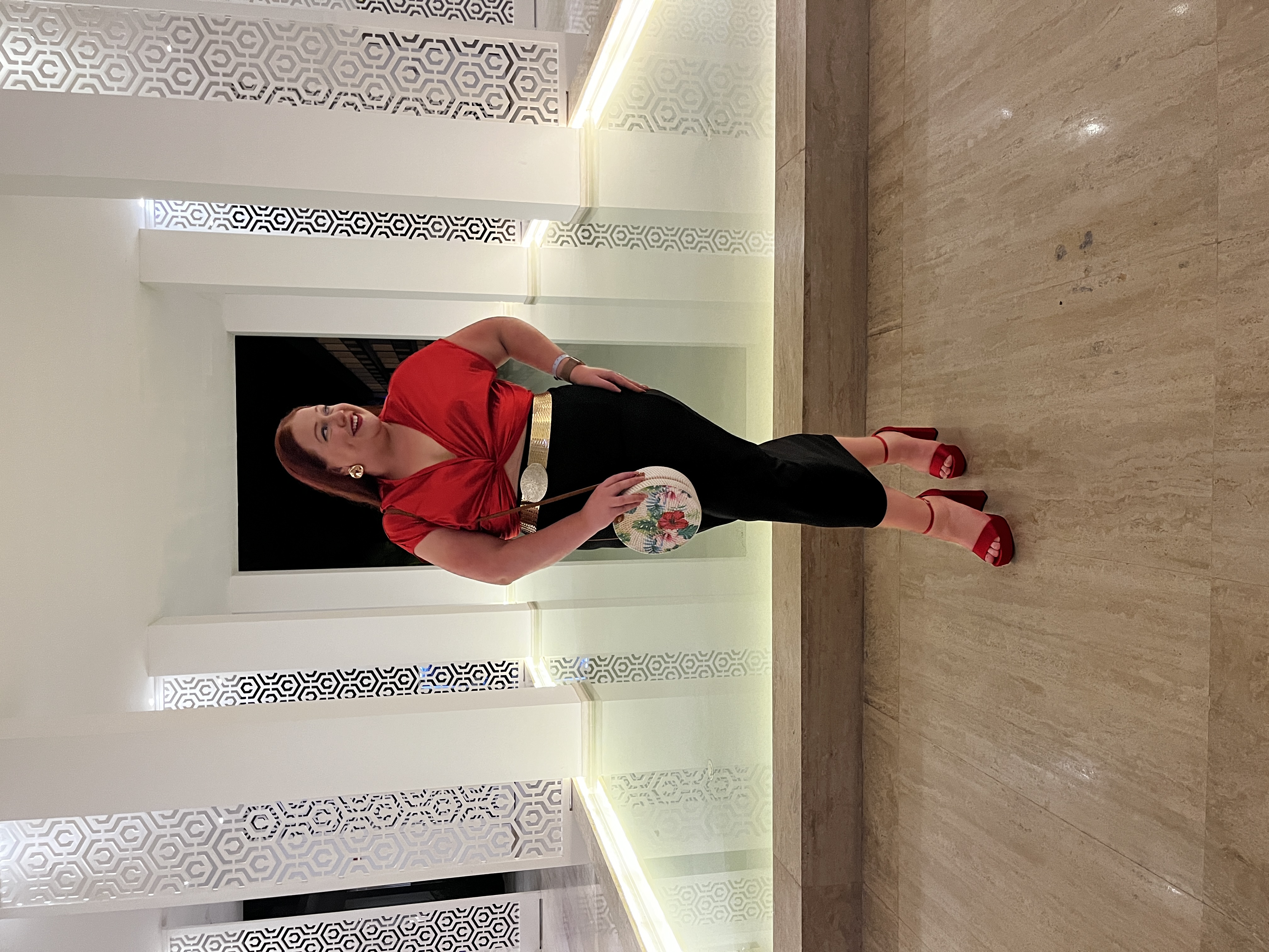 Advisor in a red shirt and matching heels posing indoors in front of a modern marble fountain