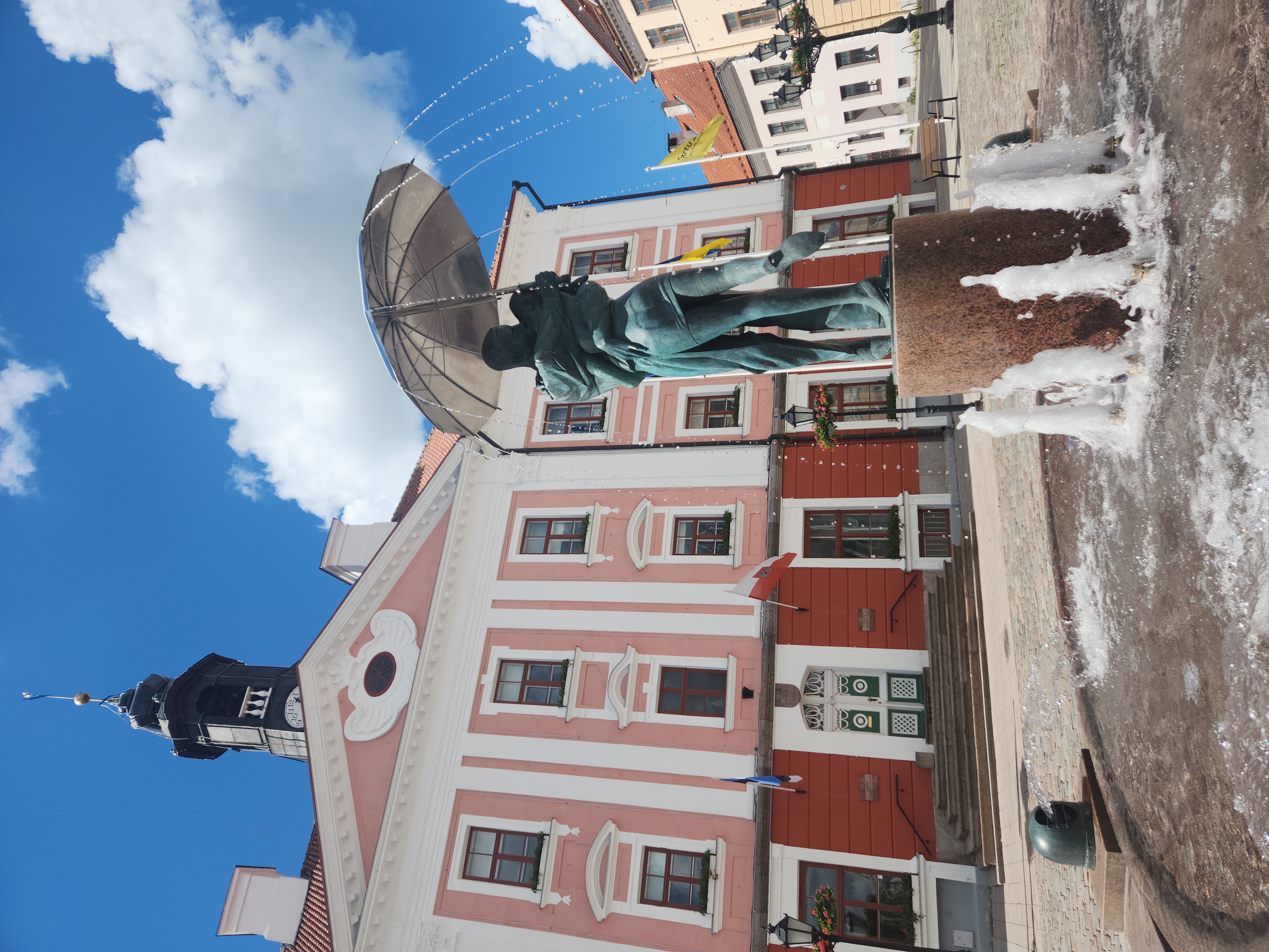 View of a statue fountain of two people embracing in front of a pink building on a sunny day