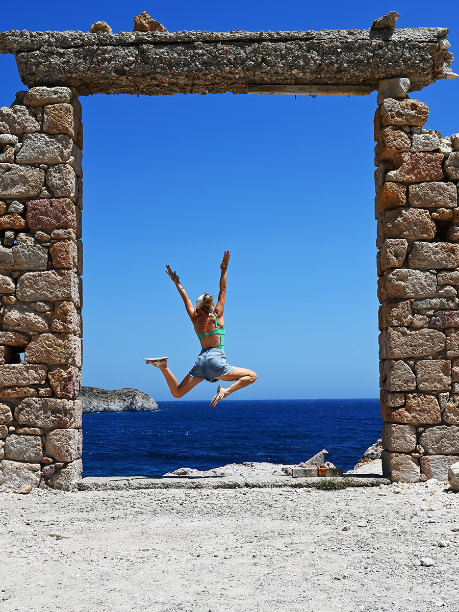 Advisor jumping in the air with arms raised underneath a stone archway overlooking the sea