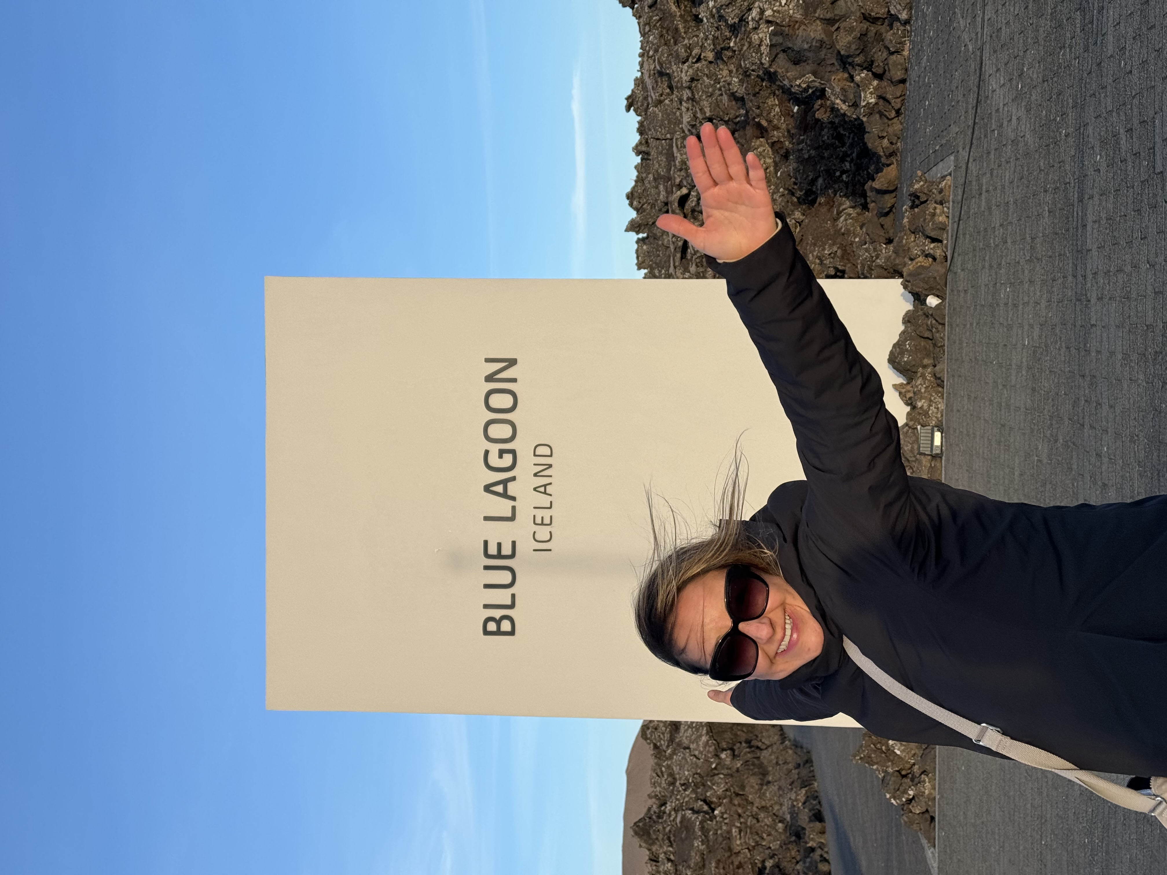 Karla posing with hands in the air in front of a sign that reads "Blue Lagoon Iceland".