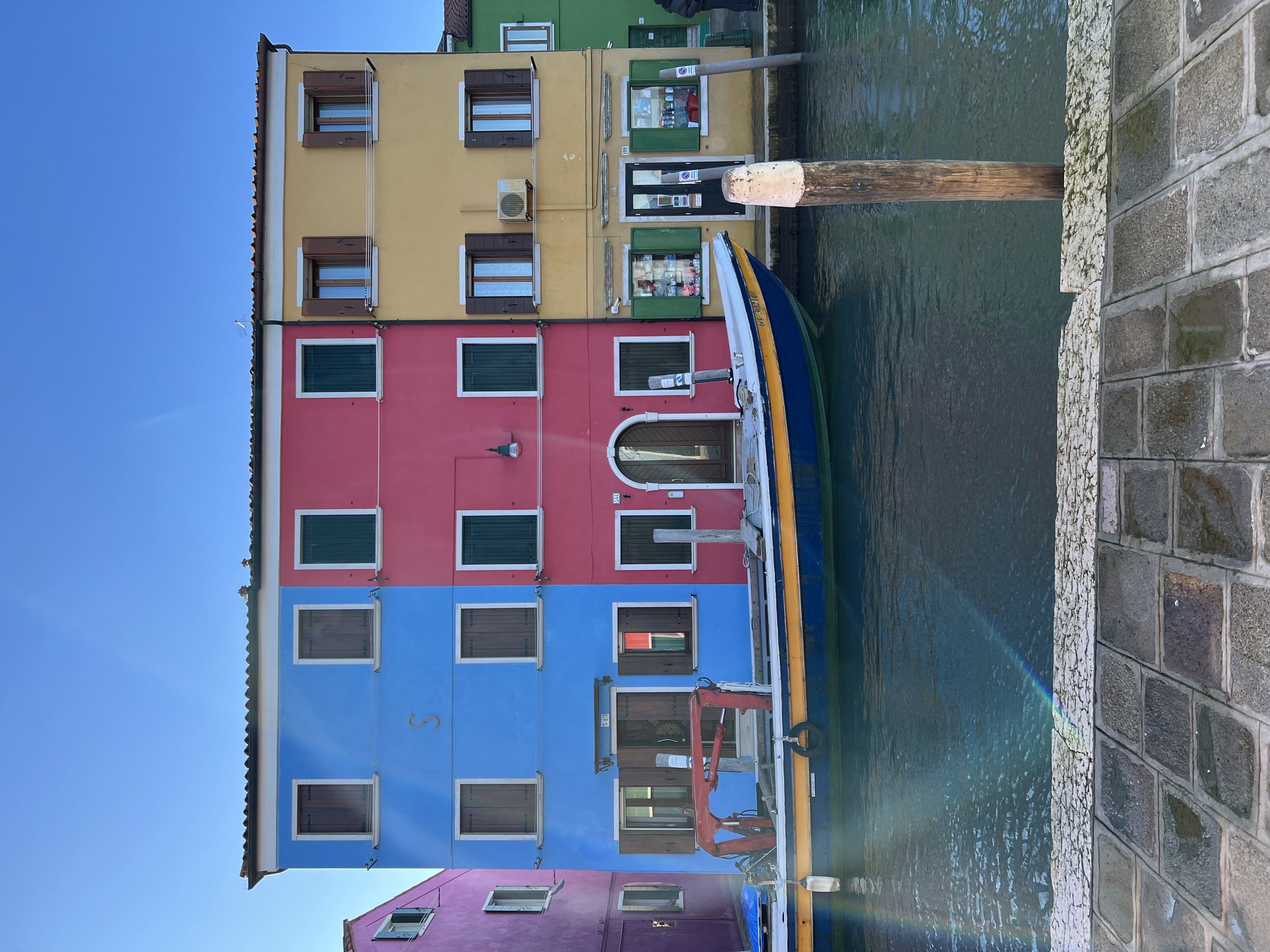A blue, red and yellow set of homes behind a canal and boat.