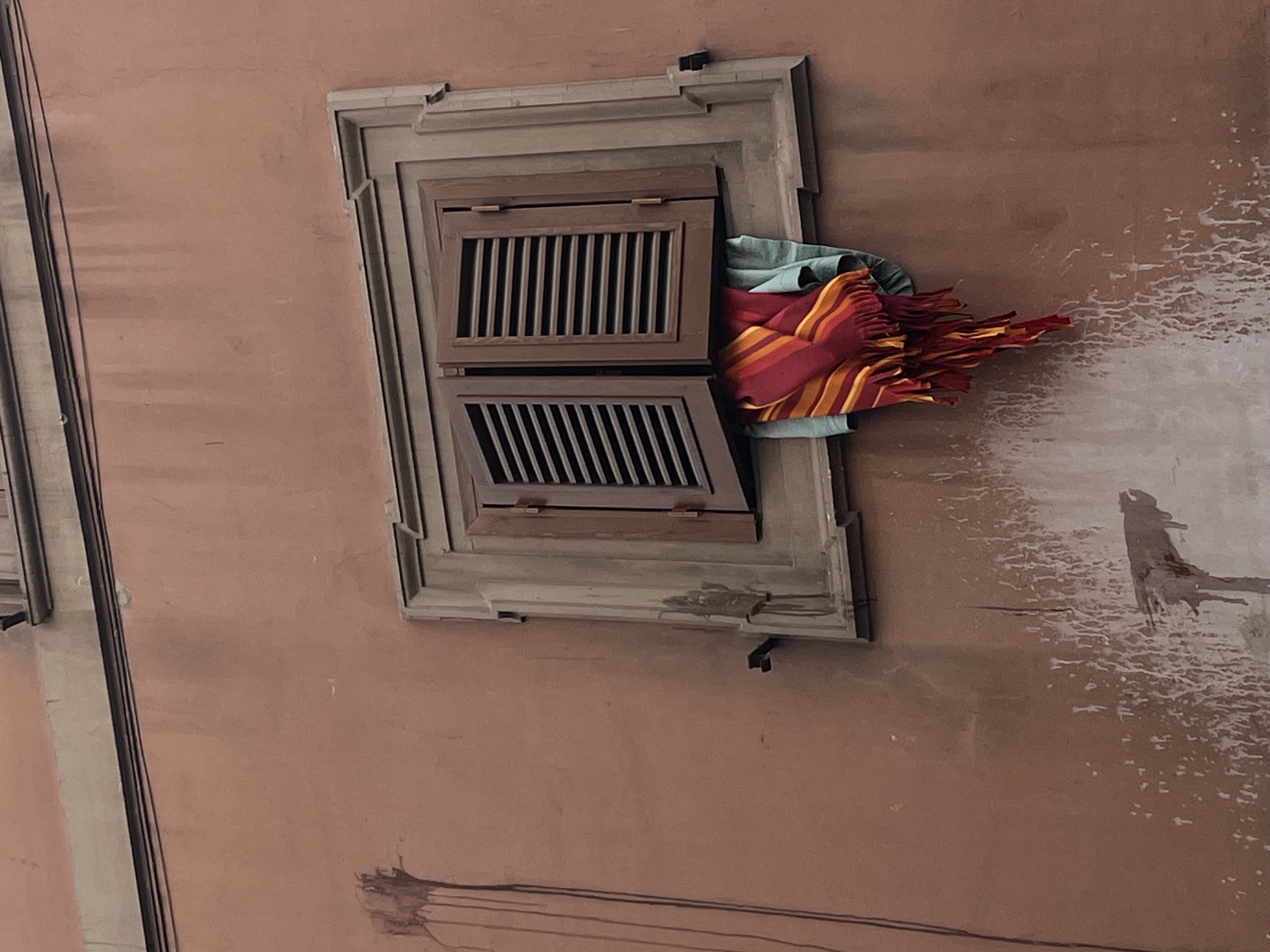 Laundry hanging out of a shuttered window.