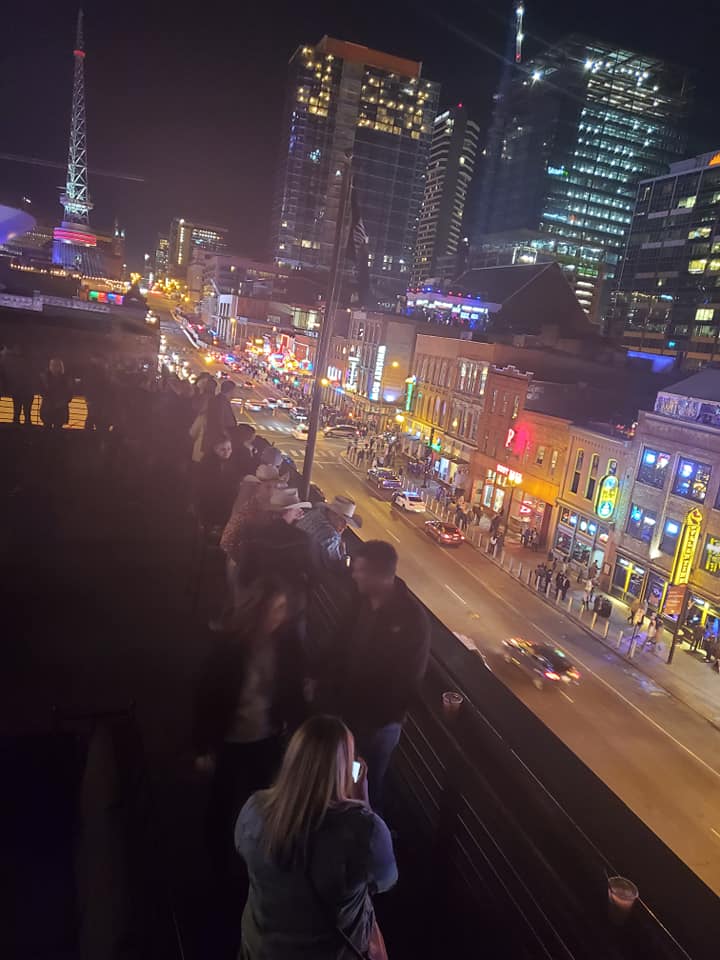 A rooftop bar at night with views of city lights in the background.