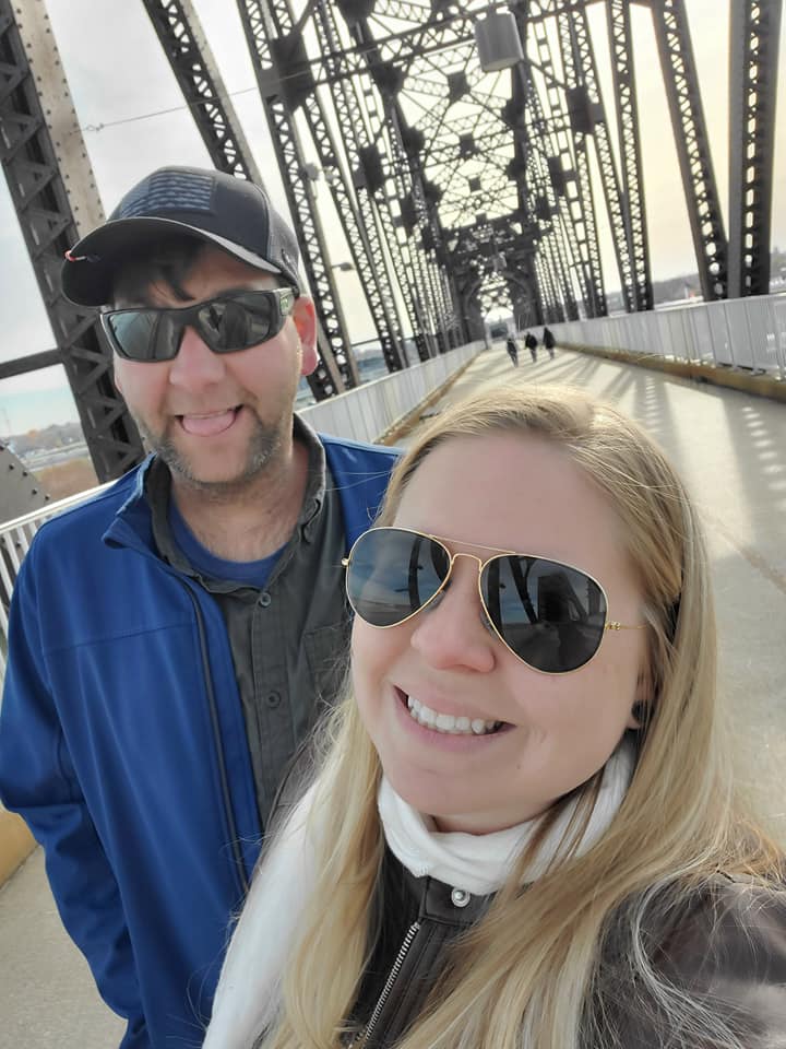 A couple posing for a selfie on a bridge outside.