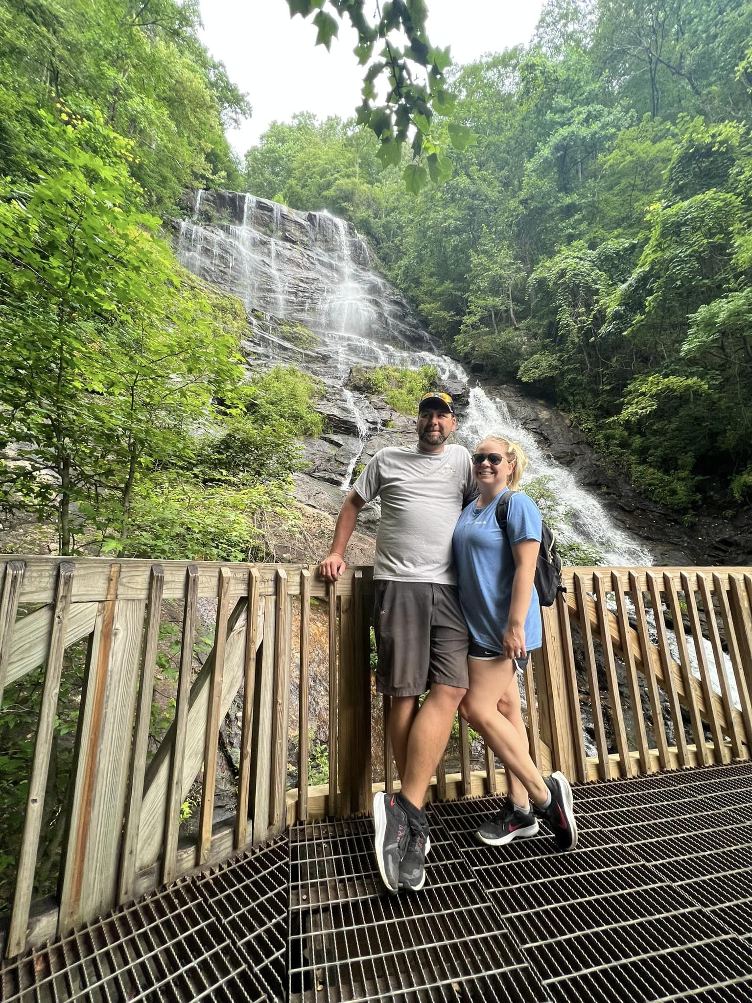 A couple posing on a bridge in front of a waterfall.