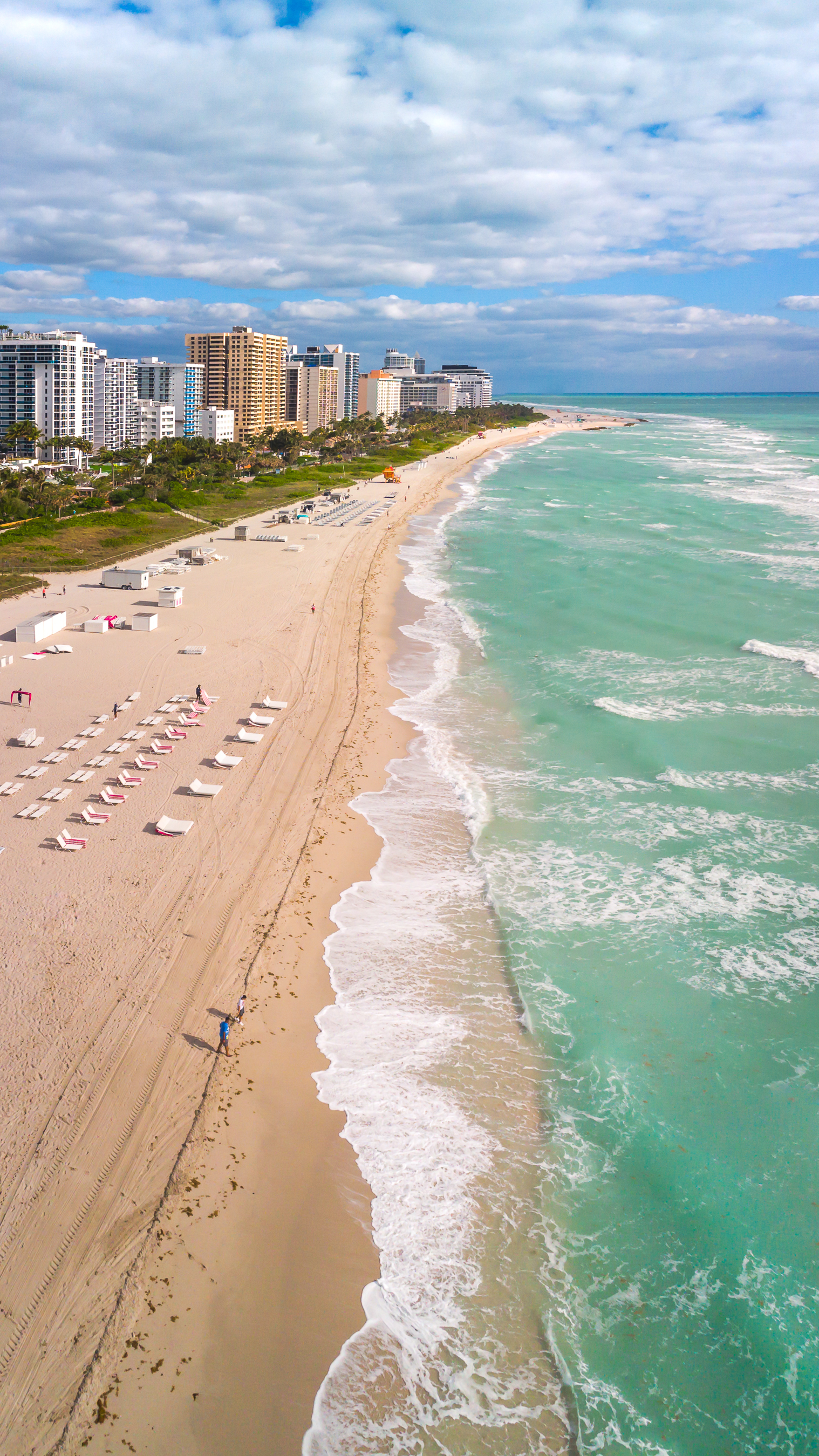A view of a sandy beach as waves lap the shore on a sunny day.