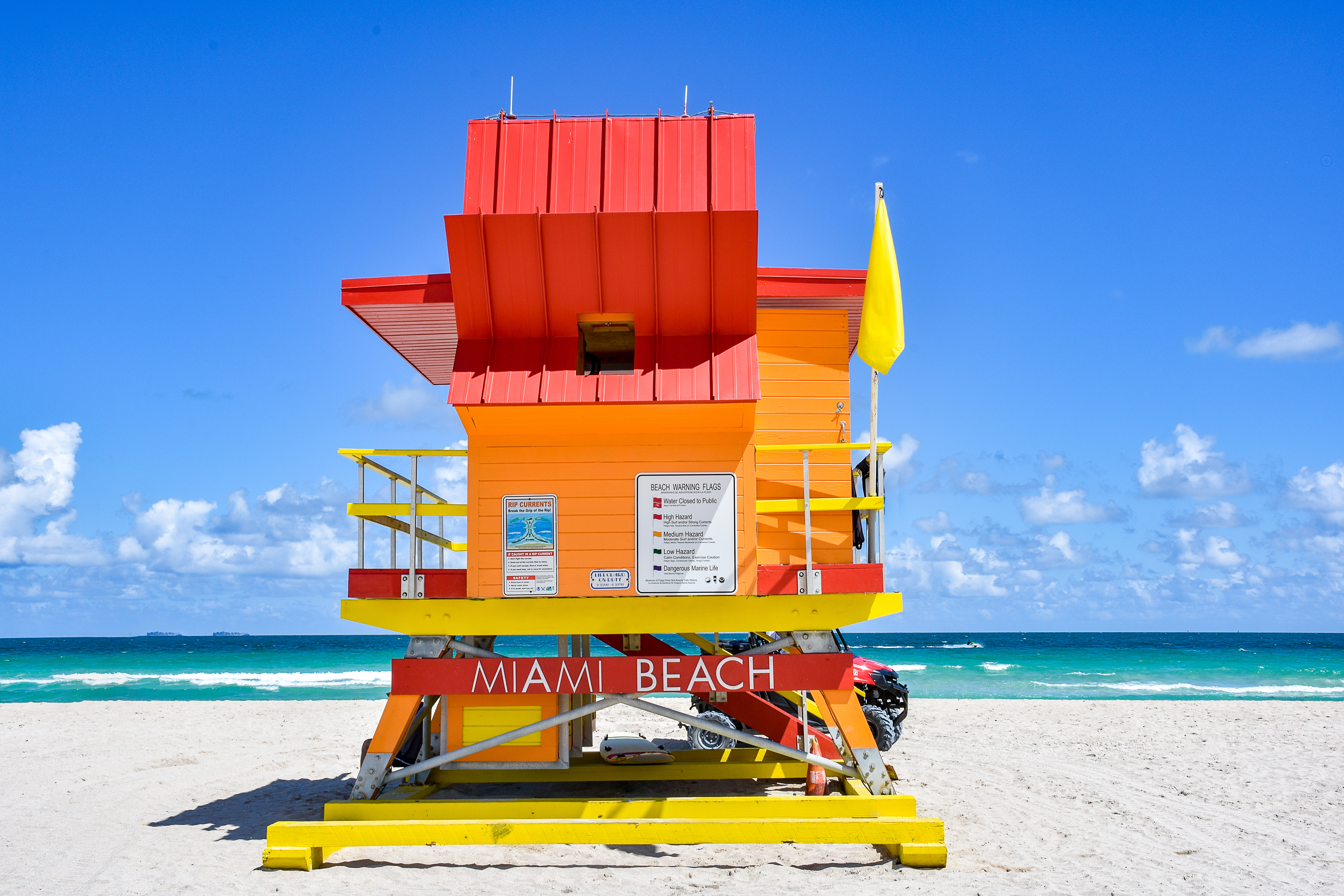 A lifeguard tower stands tall against a clear sky as waves lap the shore.