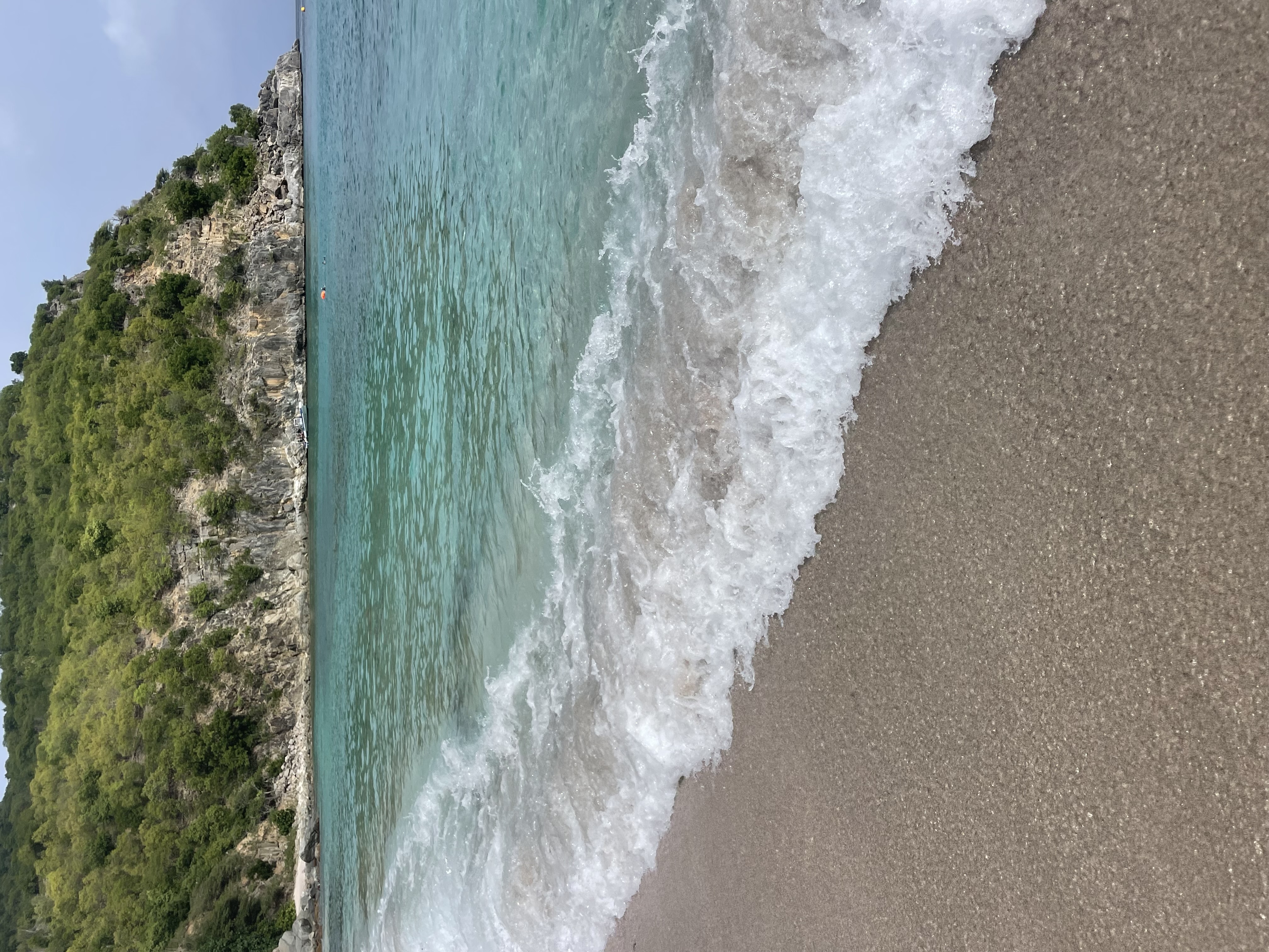 View of small waves crashing on shore with green cliffs in the background