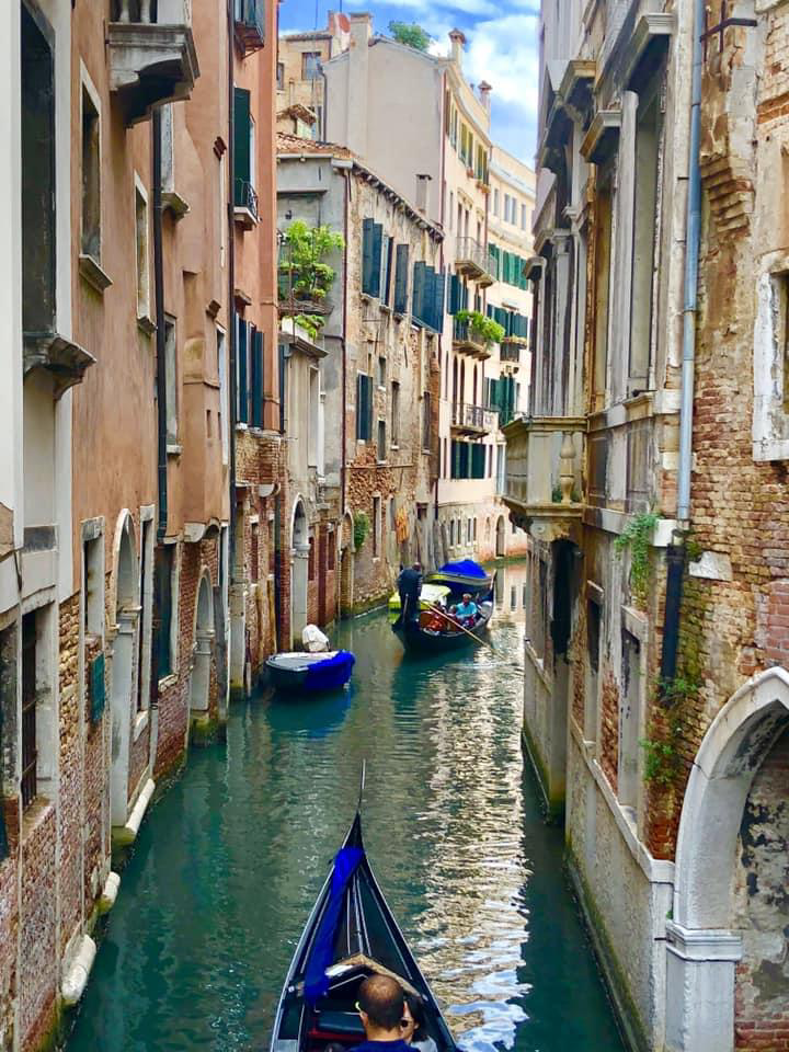 A gondola glides through a narrow canal in Venice, surrounded by historic buildings and serene waters.