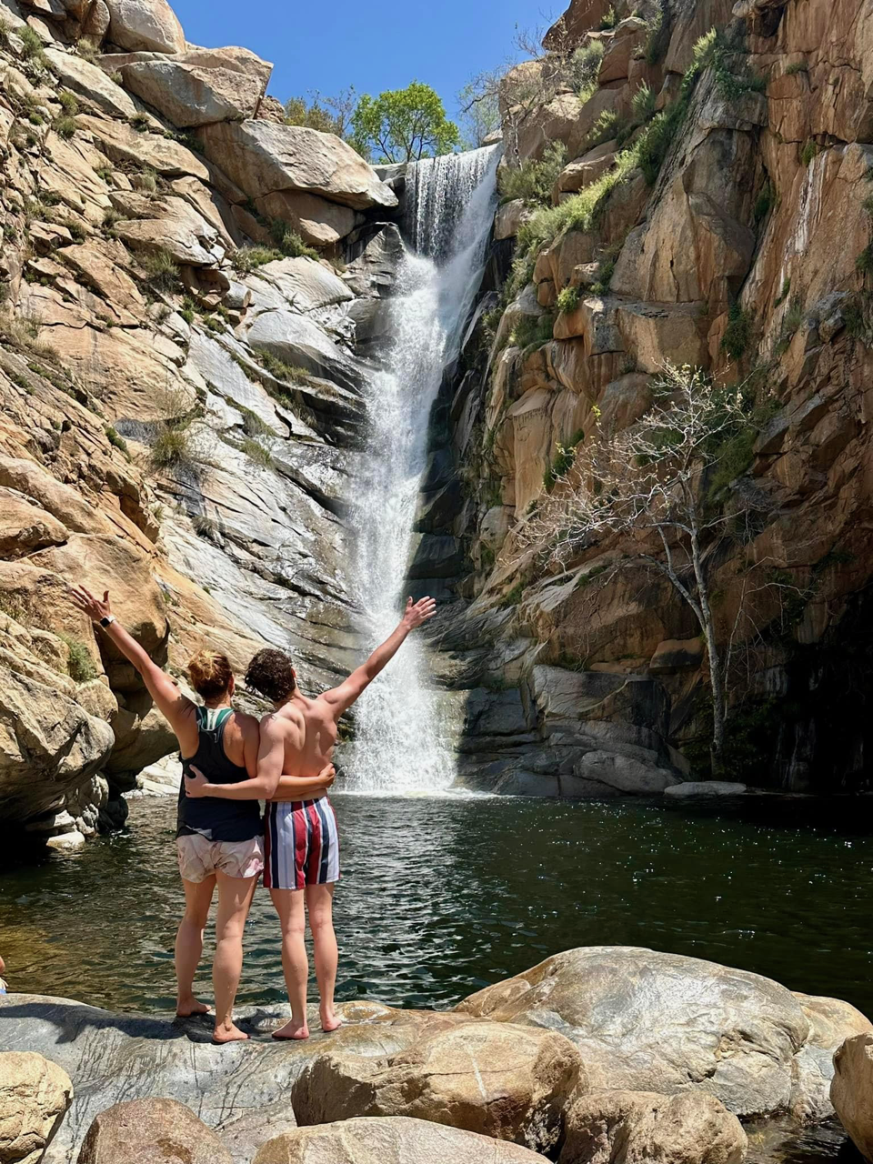 Julie and friend posing in front of a beautiful waterfall during the daytime.