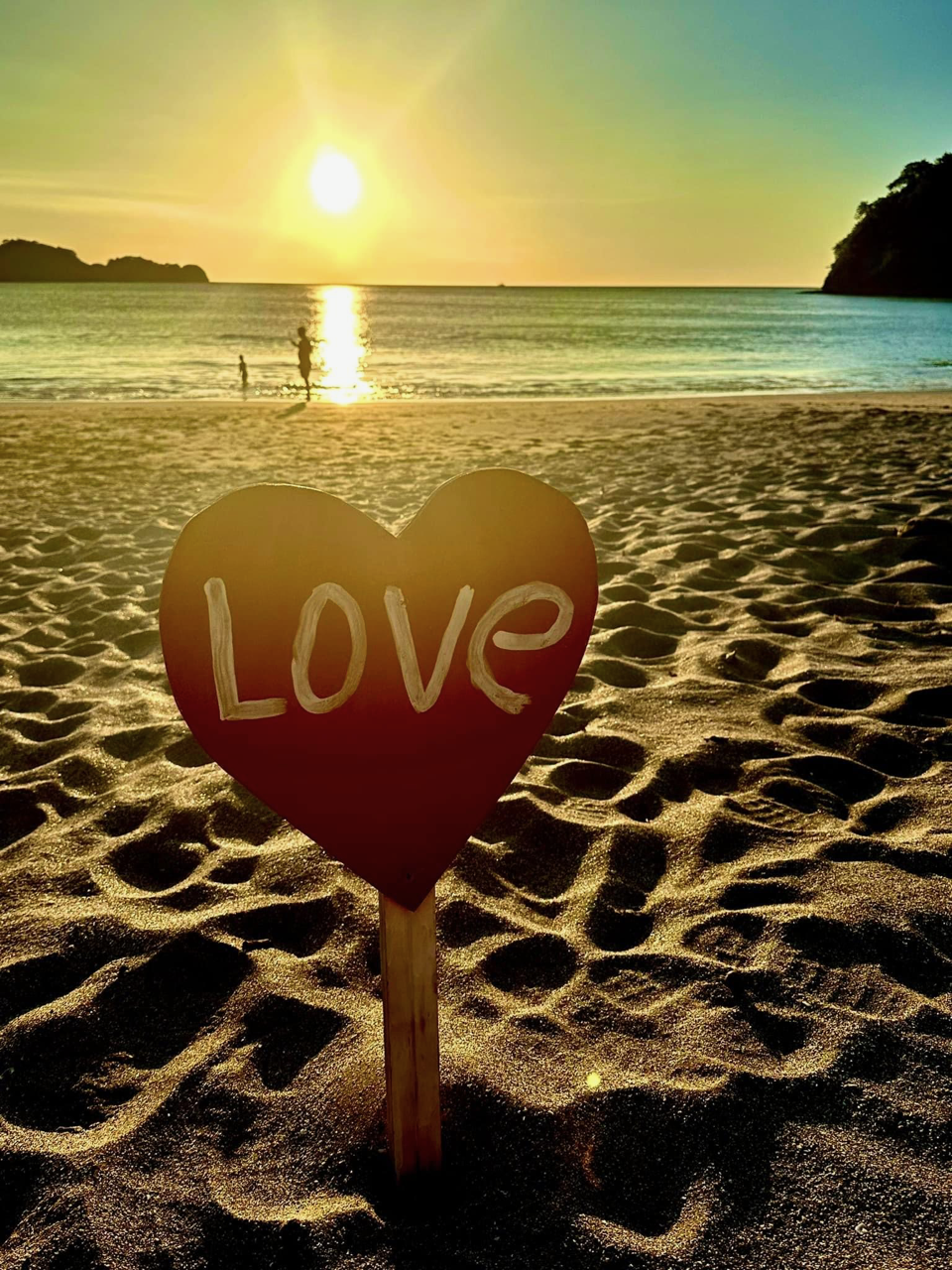 A heart-shaped love sign on the sandy beach, illuminated by the warm hues of a sunset in the background.