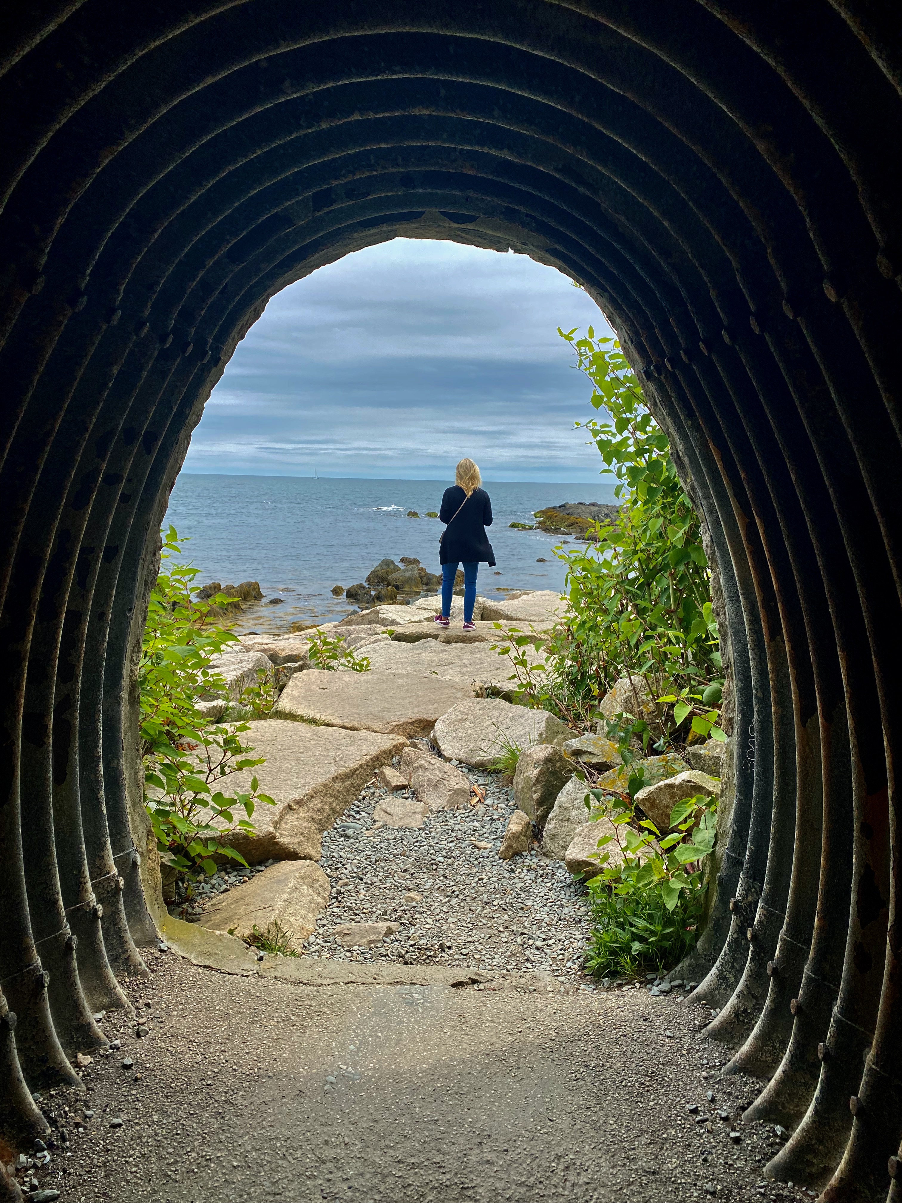 A view of a woman standing in the distance at a look out point with the ocean on a cloudy day.