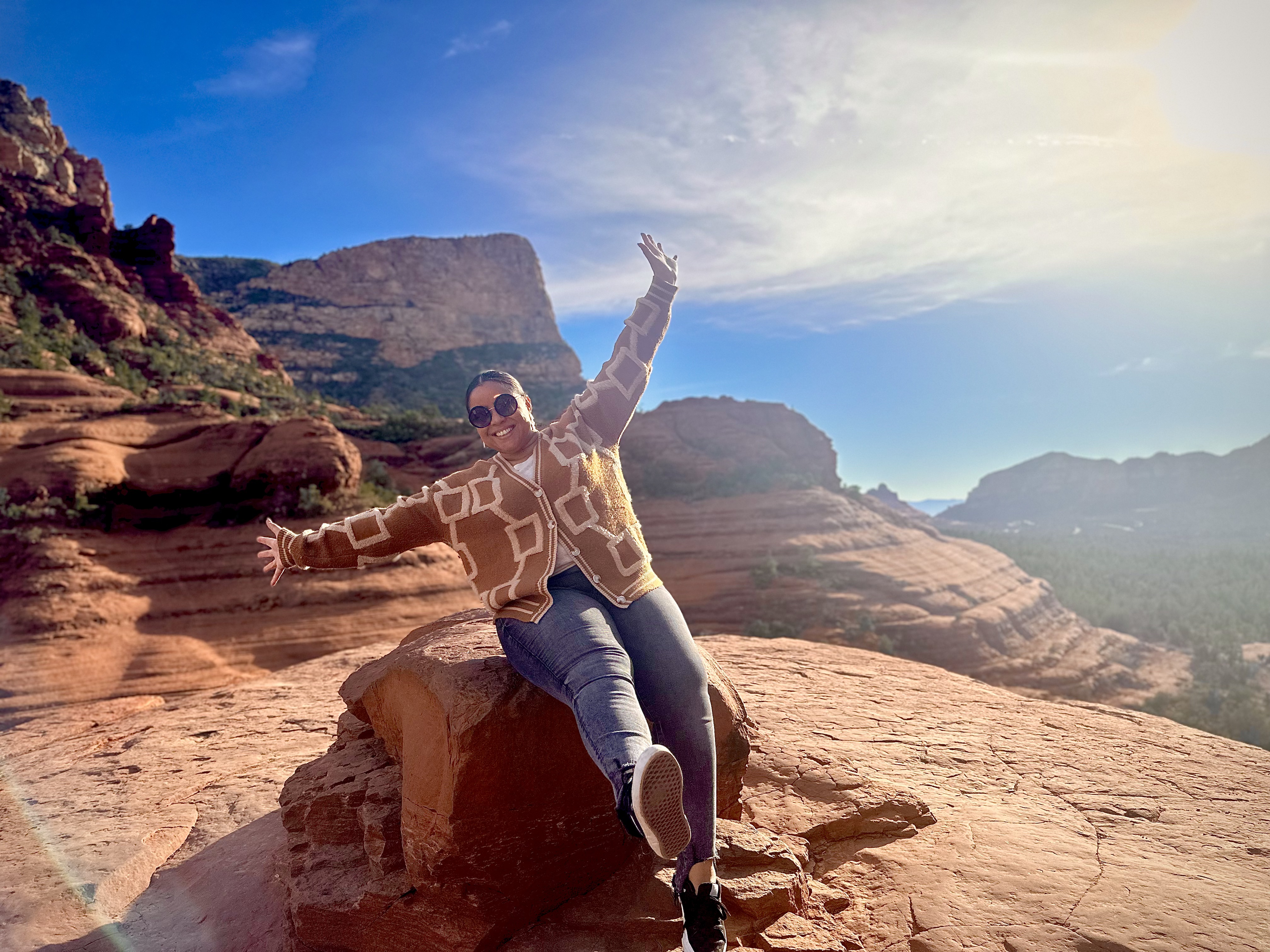Advisor sitting on a red rock with arms raised overlooking a beautiful canyon