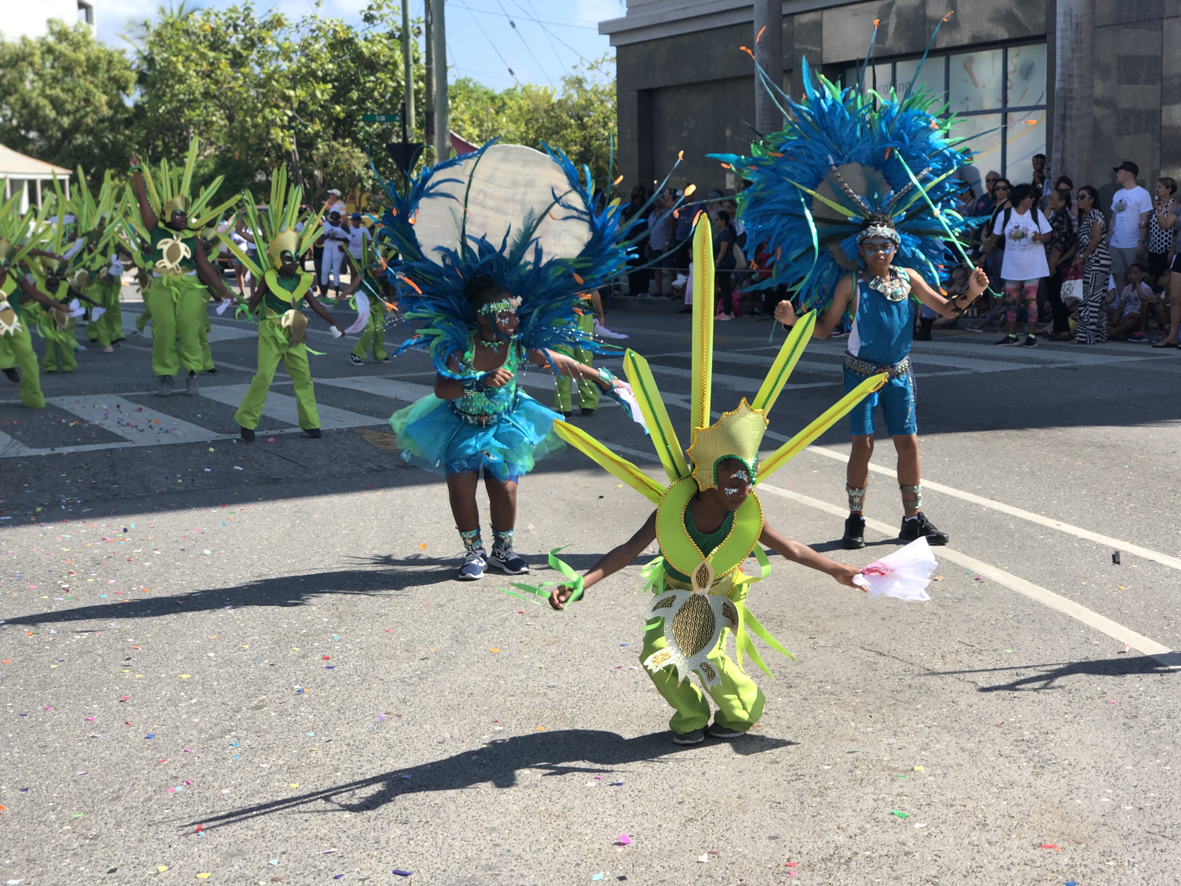 A parade of participants in brightly colored costumes dancing in the street on a sunny day.