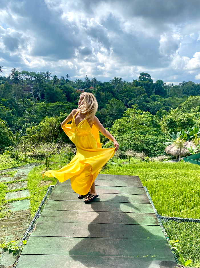 A person twirling in a long yellow dress in a field during the daytime