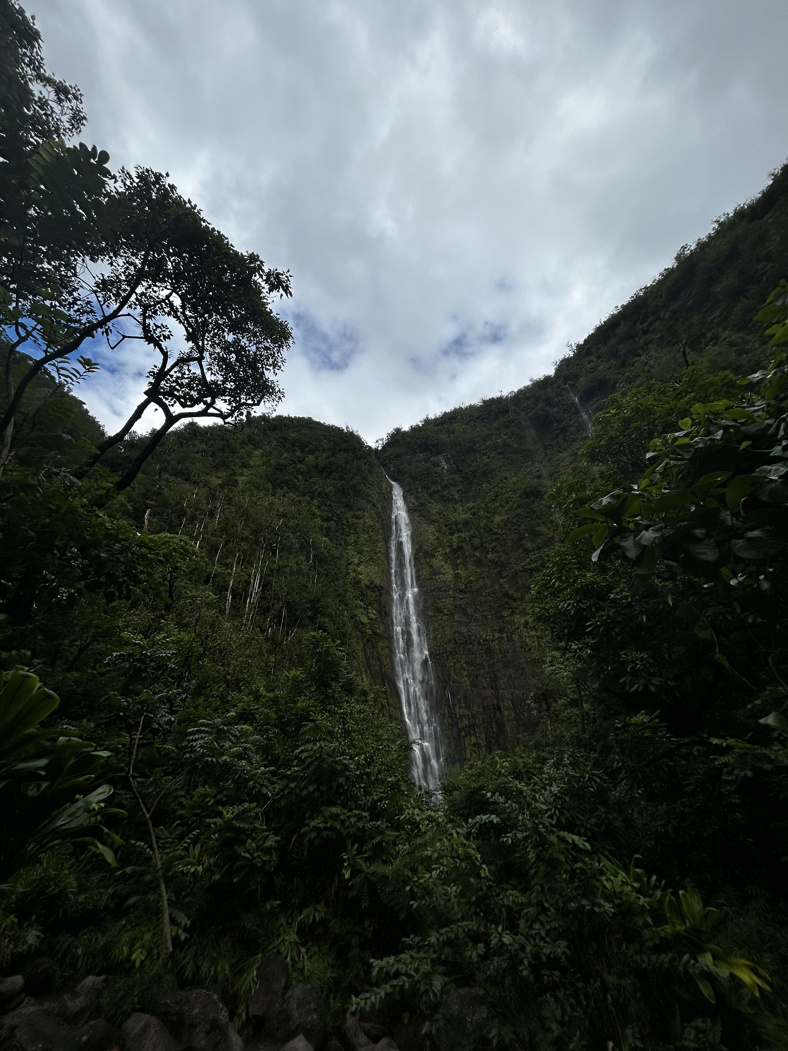 View of a tall waterfall in a lush jungle under cloudy skies