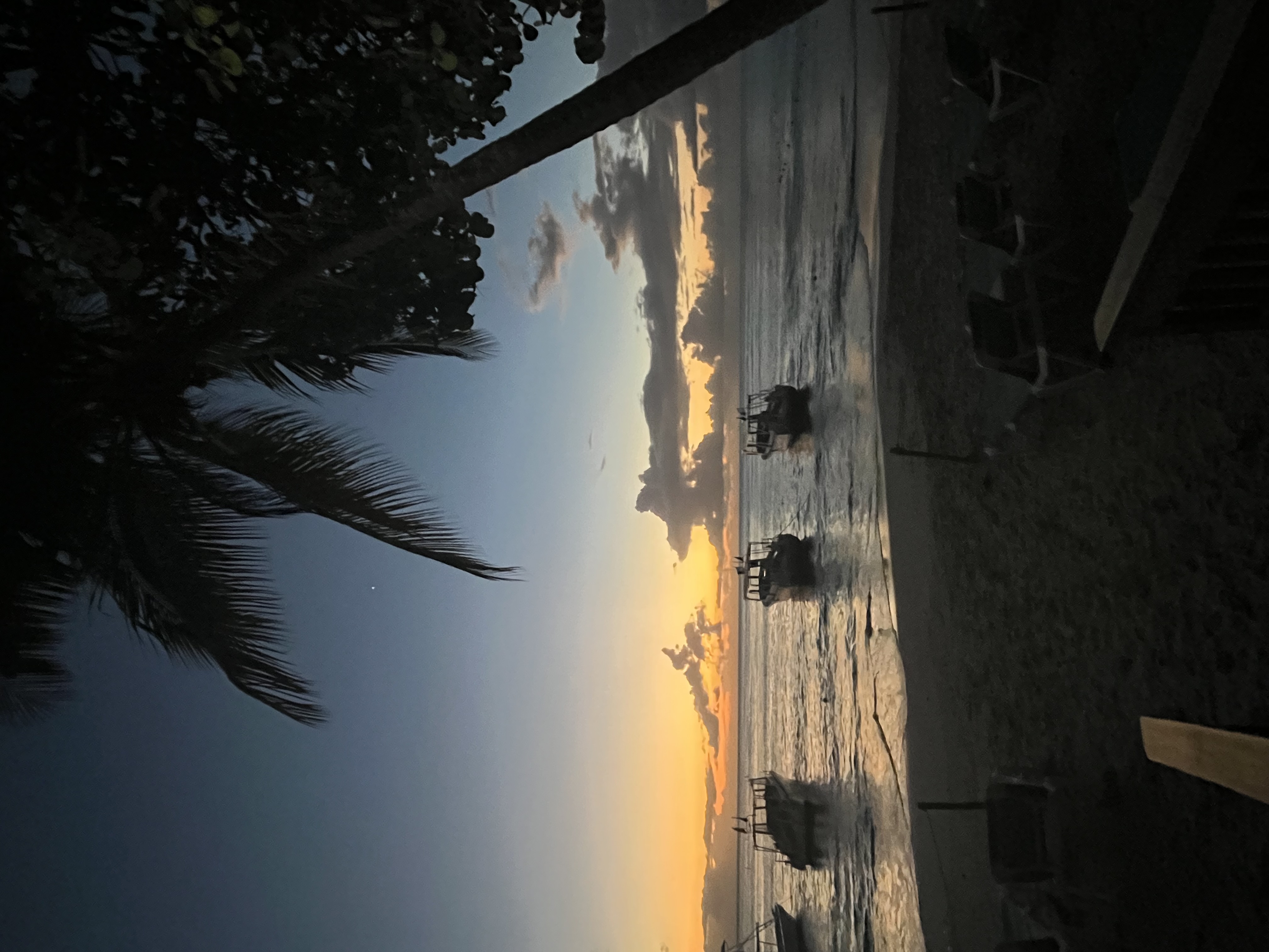 Serene photo of the beach with boats in the water during sunset.
