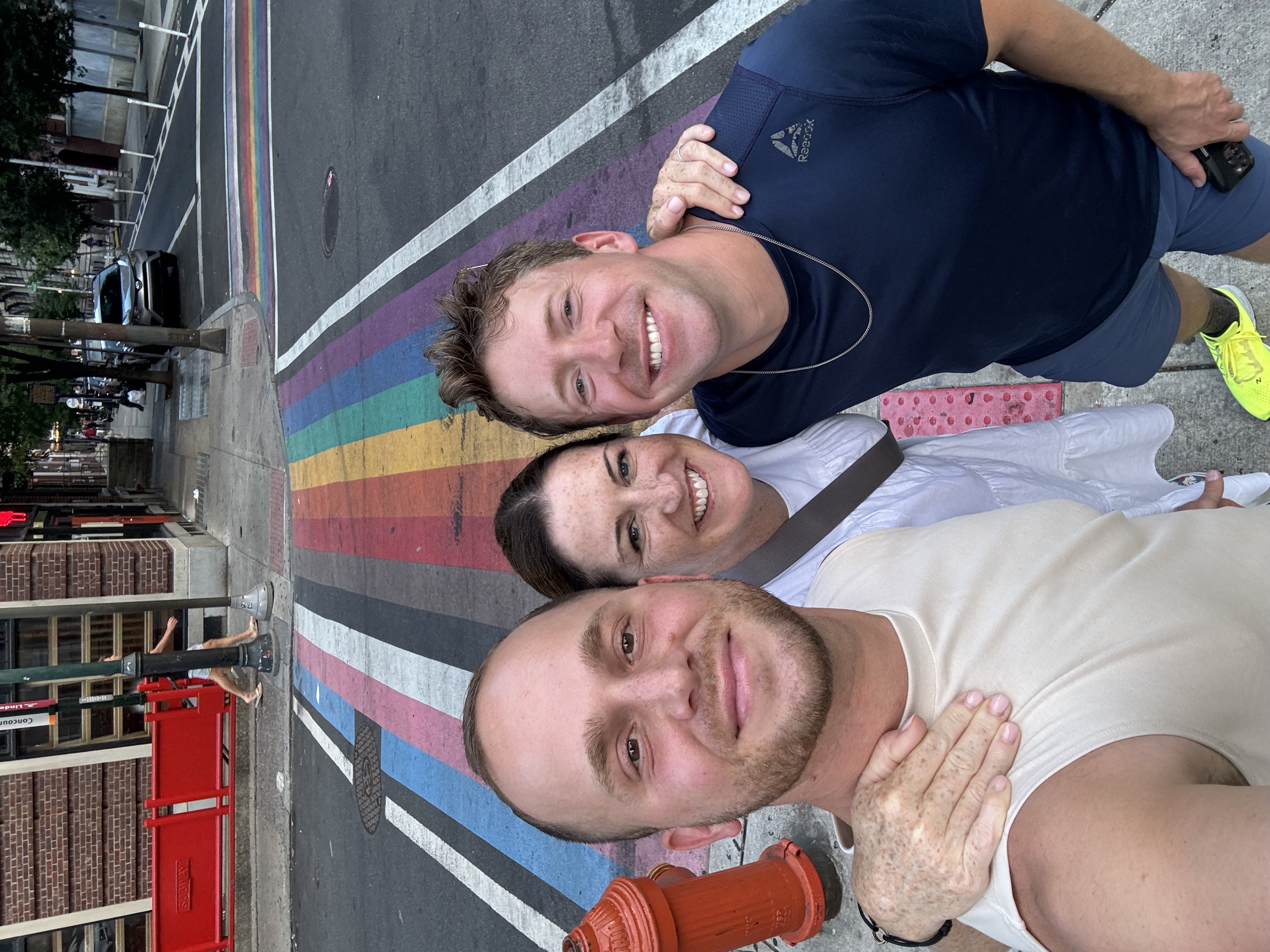 Jeffrey posing with friends outdoors with a pride flag painted on the road.