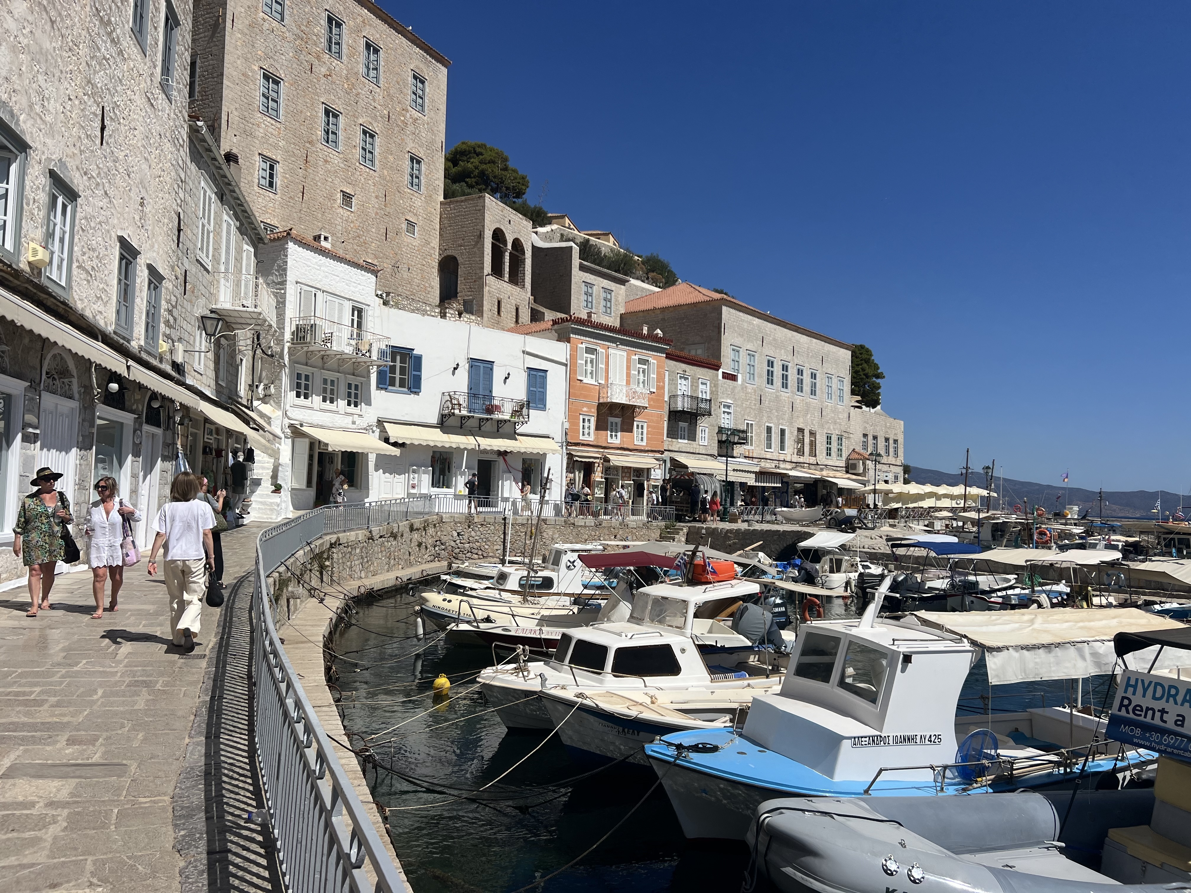 View of a marina filled with small boats and people walking along a promenade on a clear day