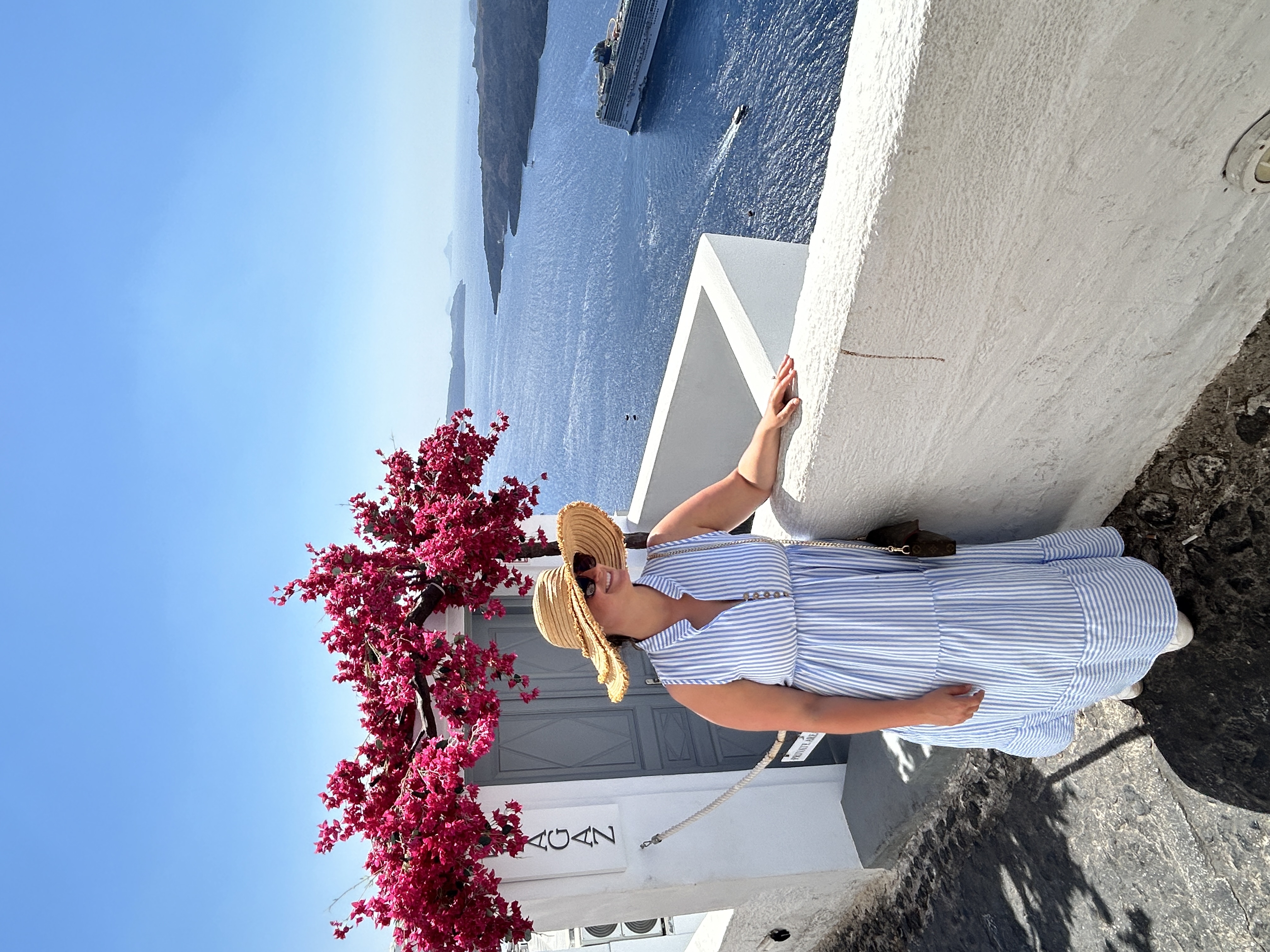 View of advisor posing by a white wall and pink flowers overlooking the sea on a sunny day
